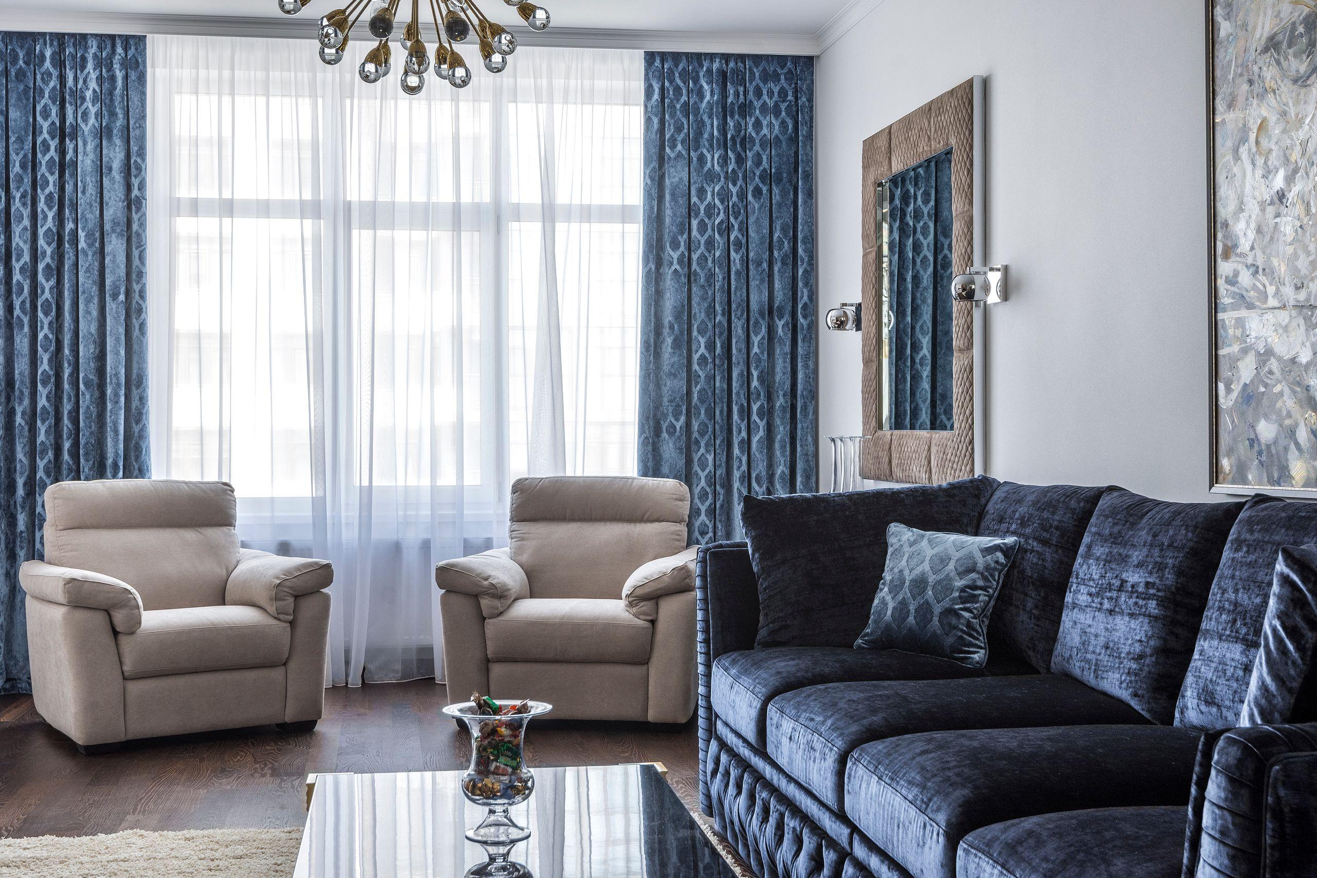 A bright sitting room with a navy sofa, cream armchairs, and tall windows dressed in sheer curtains