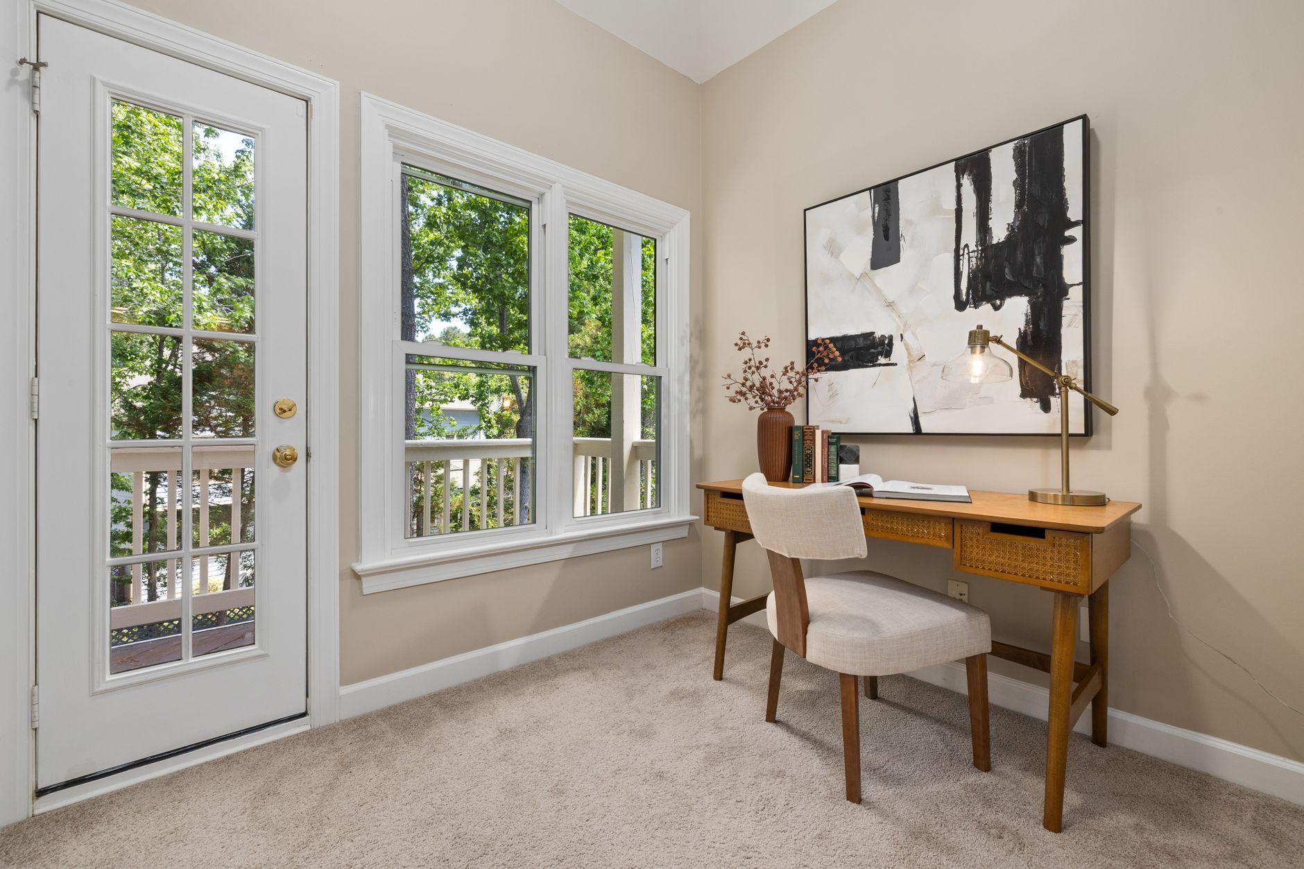 A bright home study with a wooden writing desk, cane chair, and a glass door opening onto green trees