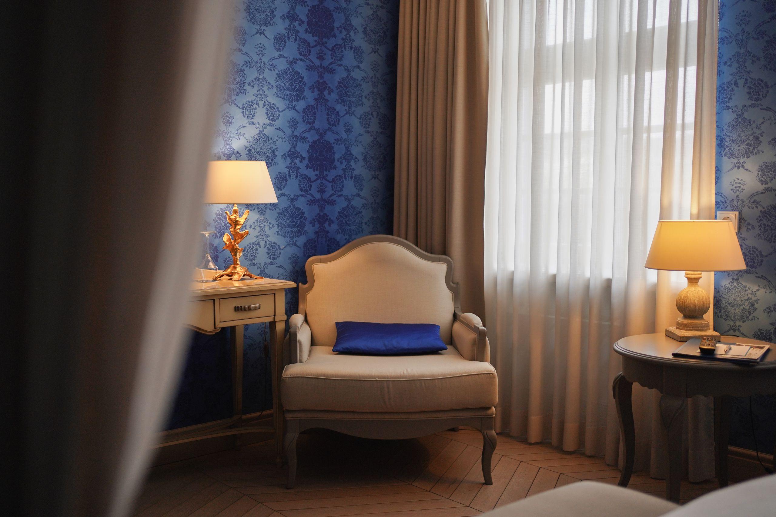 A warm sitting area with an upholstered armchair beside a tall sunlit window with soft curtains