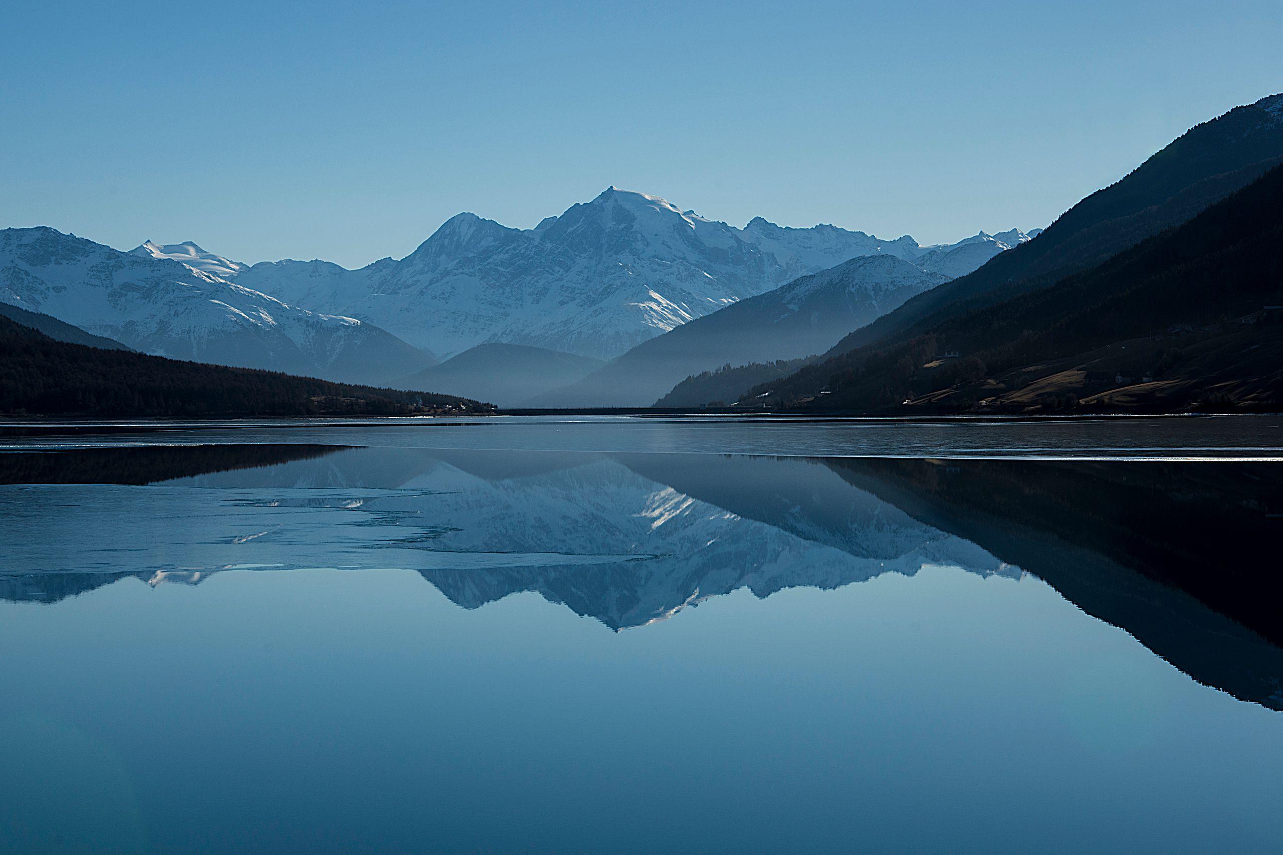 Snow-capped mountains reflected in the still, calm water of an alpine lake