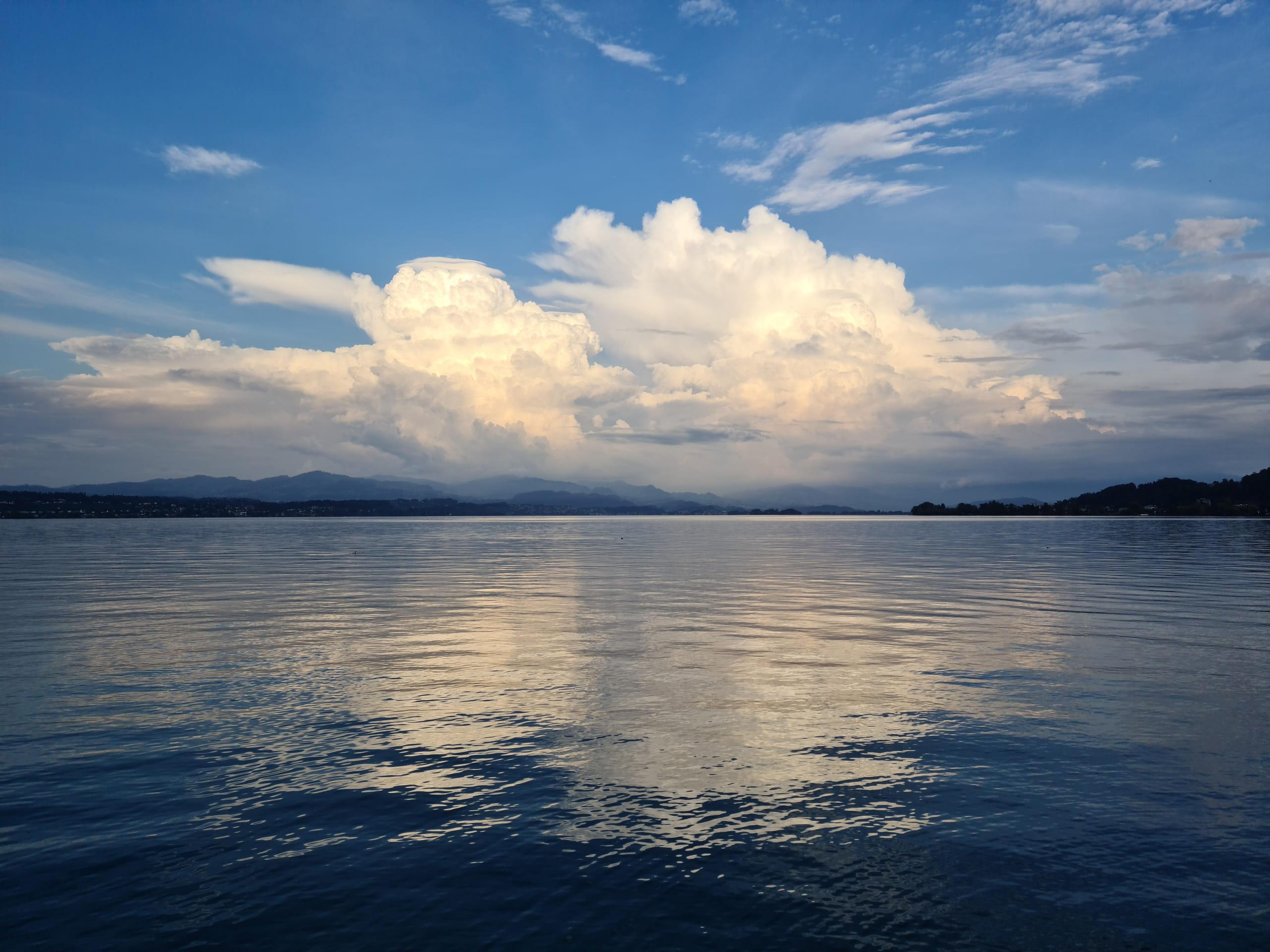 Evening light and a tall bank of cloud over the calm water of a Swiss lake