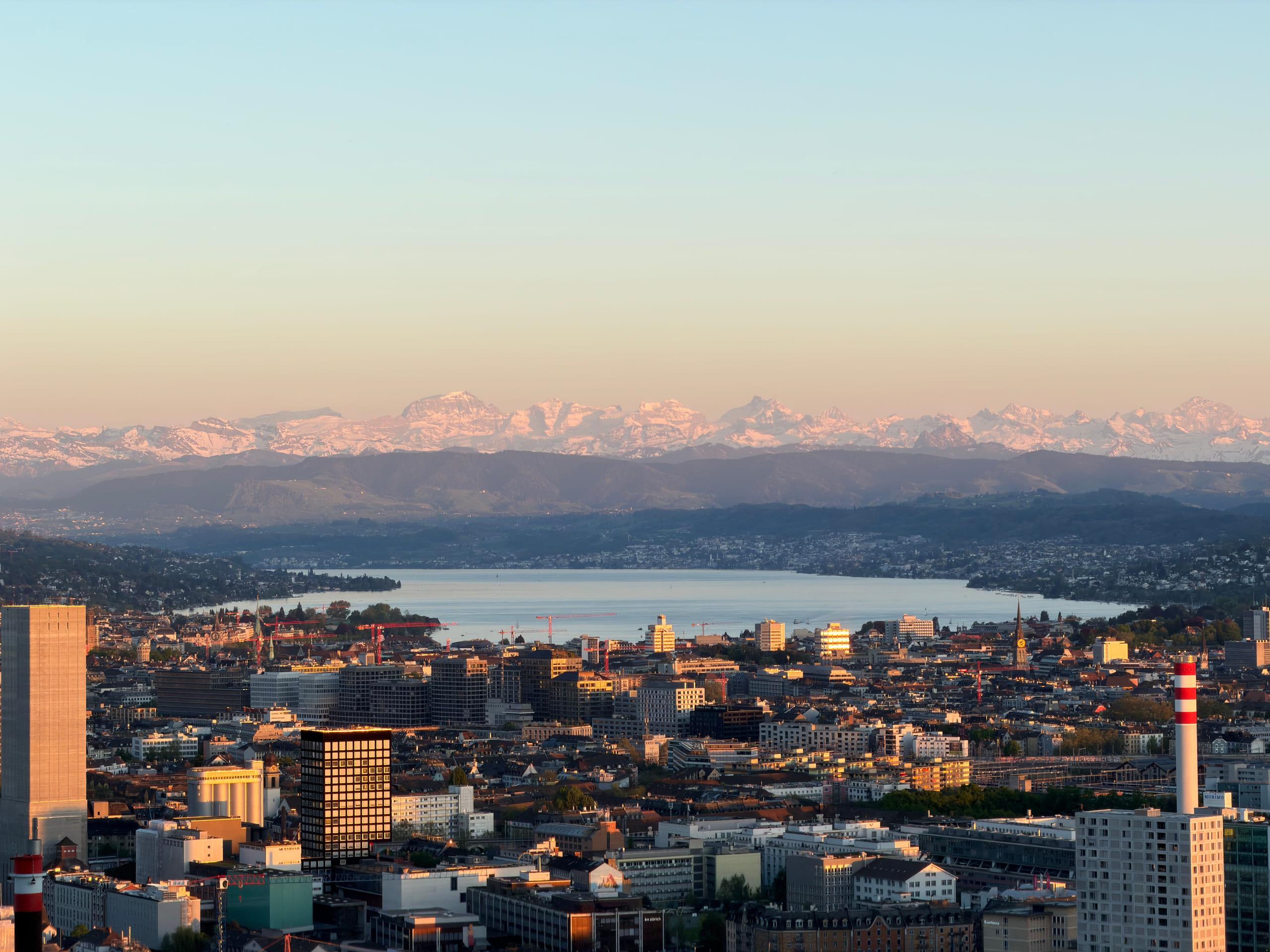 Zurich seen from above with Lake Zurich beyond it and the snow-covered Alps catching the last light