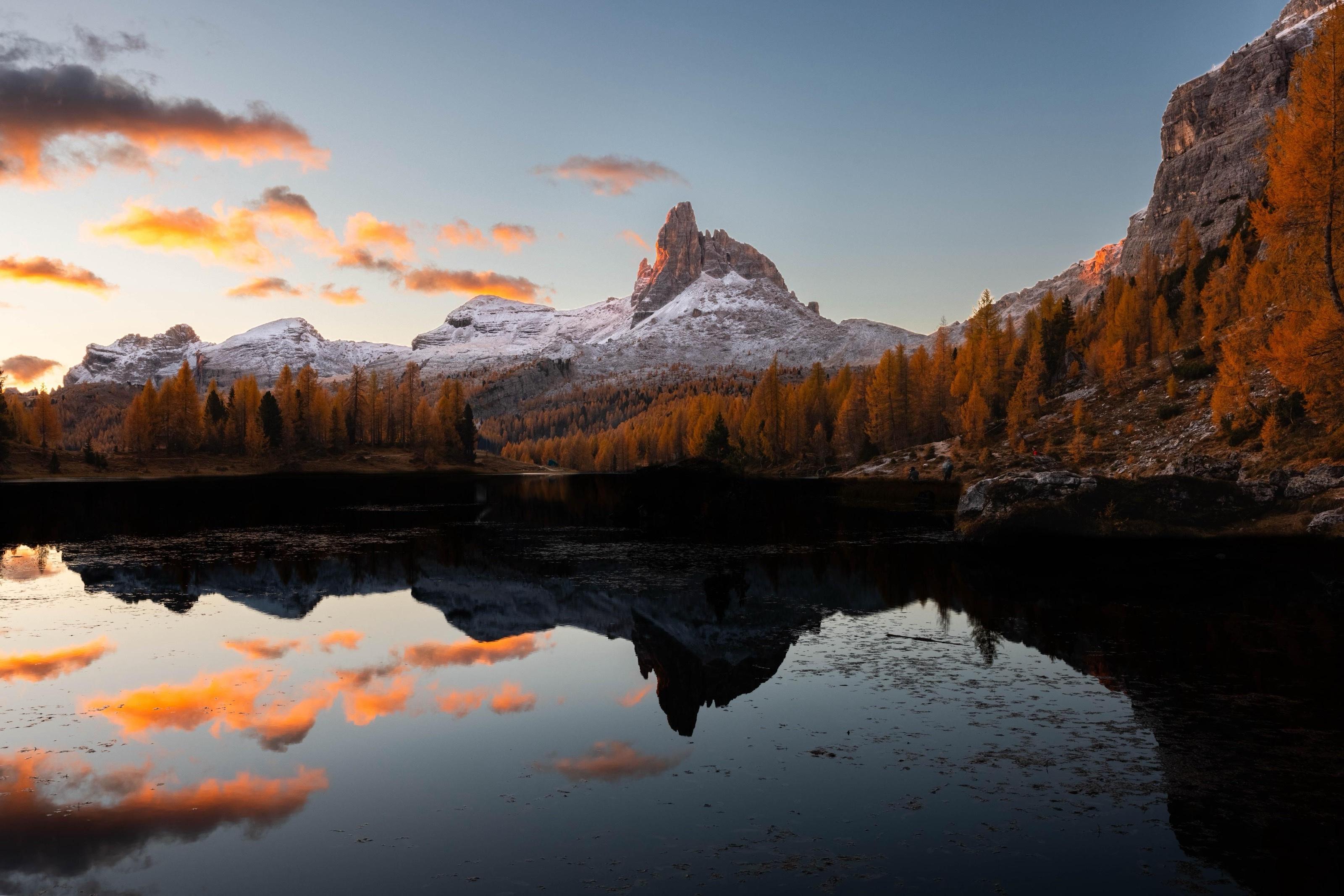 Snow-dusted alpine peaks and golden autumn larches reflected in a mirror-still mountain lake at sunrise in the Alps