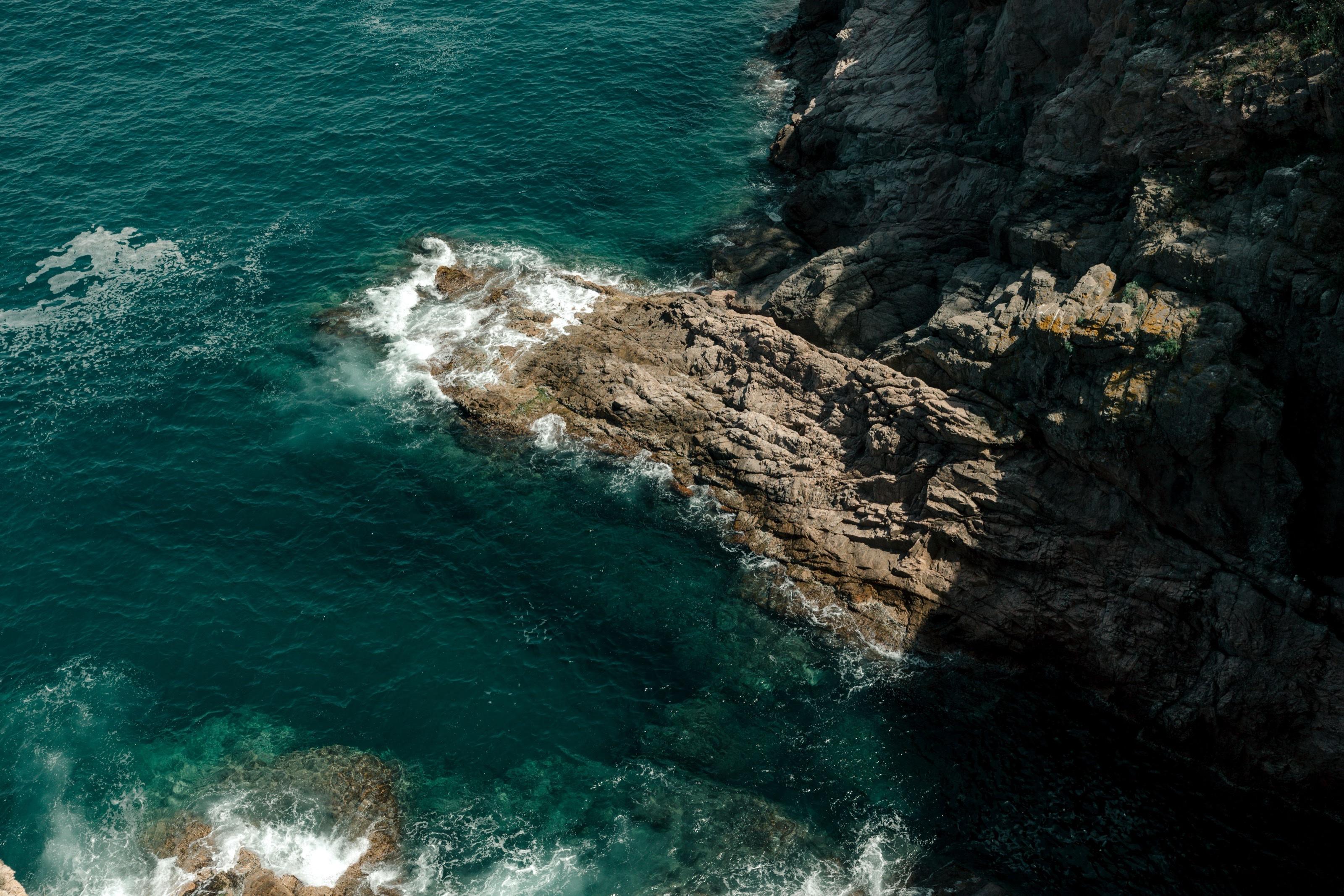 Aerial view of deep teal water meeting the rocky coastline at Tossa de Mar on Spain's Costa Brava