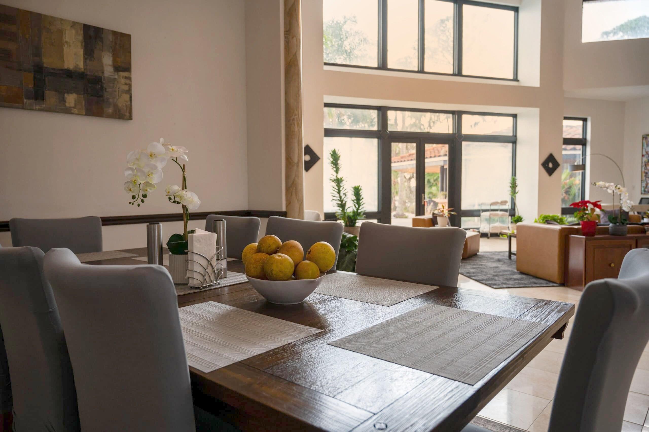 The dining room at Tikvah Lake Recovery, a long table set with orchids and a bowl of oranges beneath tall windows onto the garden