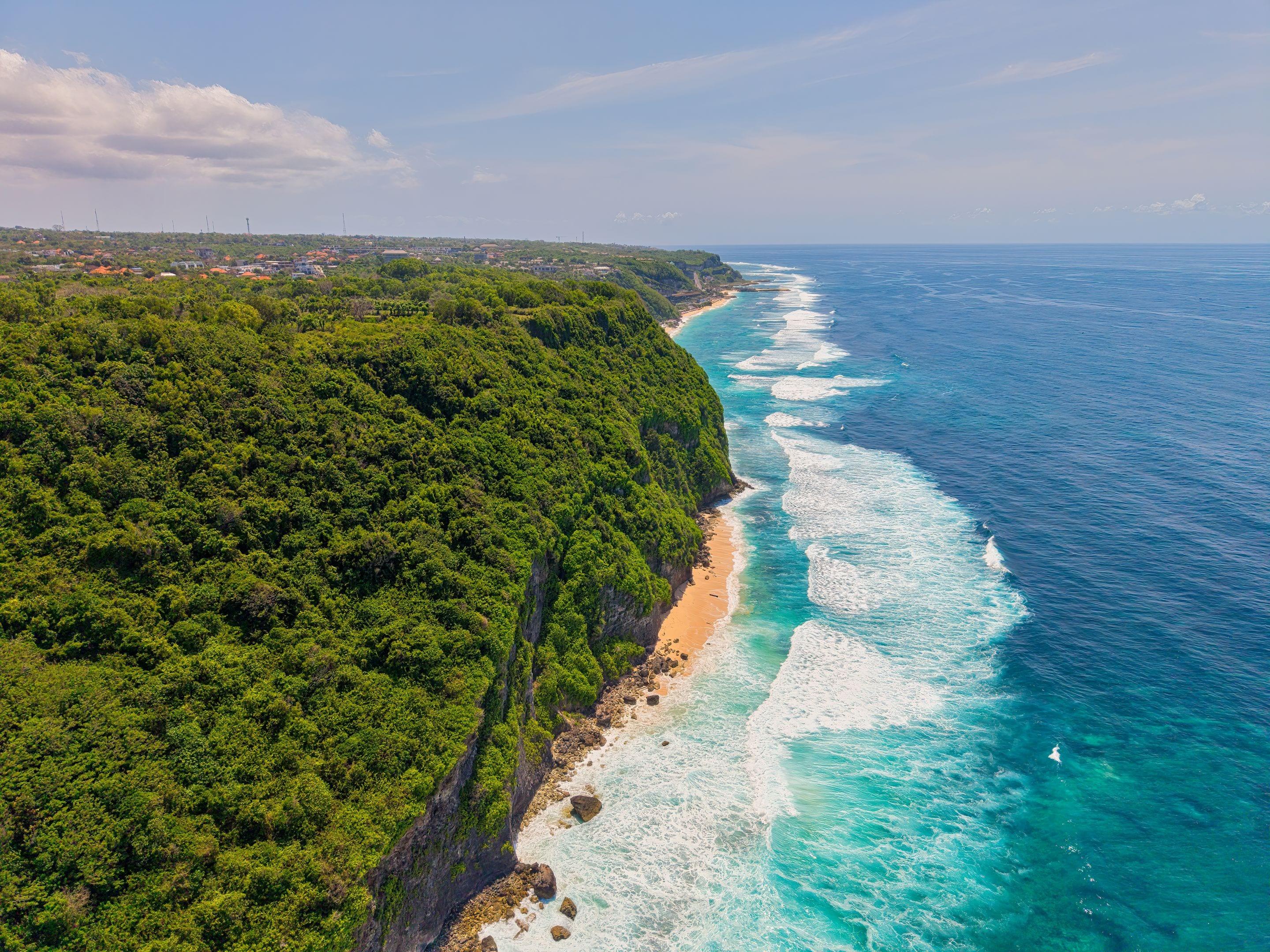 A green headland falling to bright turquoise surf on a clear day