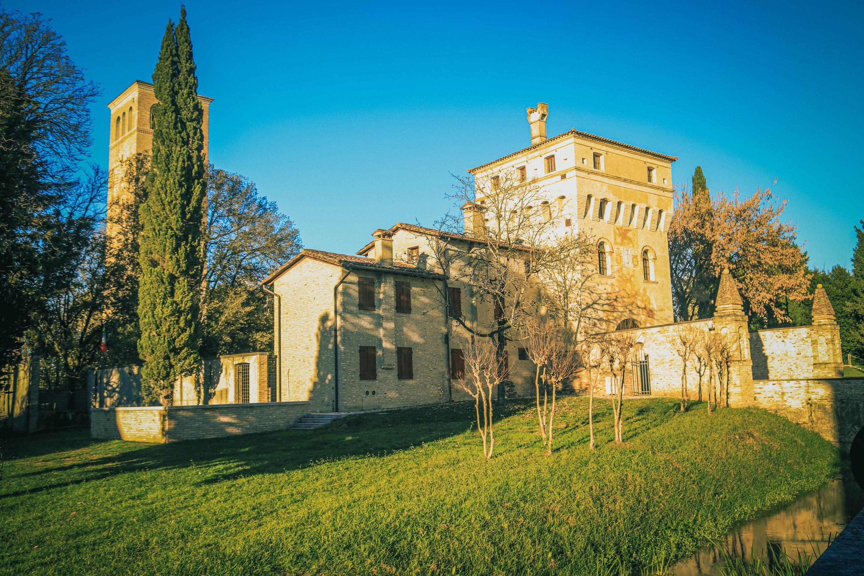 A pale stone villa on a green slope with cypresses, lit by low sun under a blue sky
