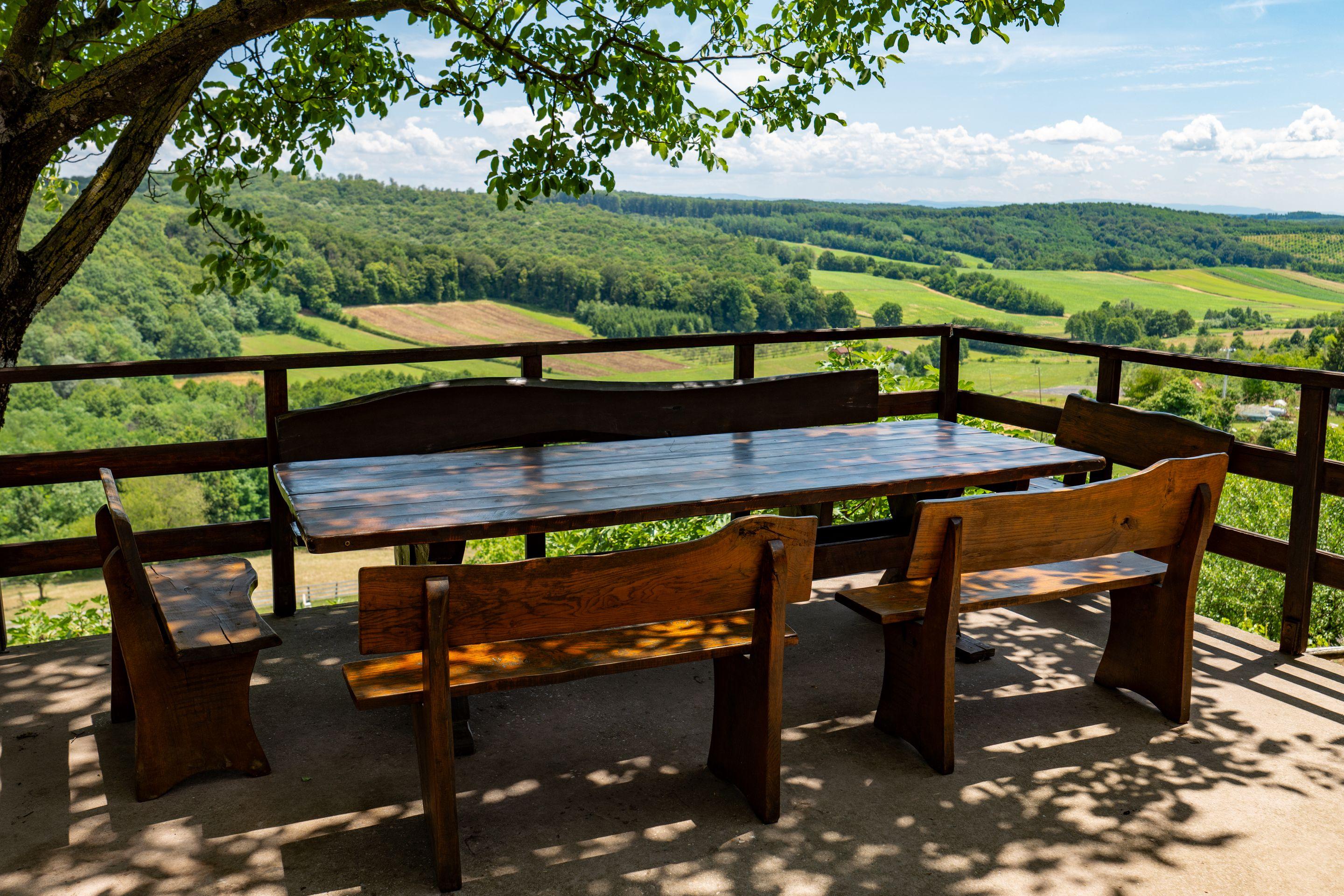 A long wooden table and benches on a terrace looking out over green farmland