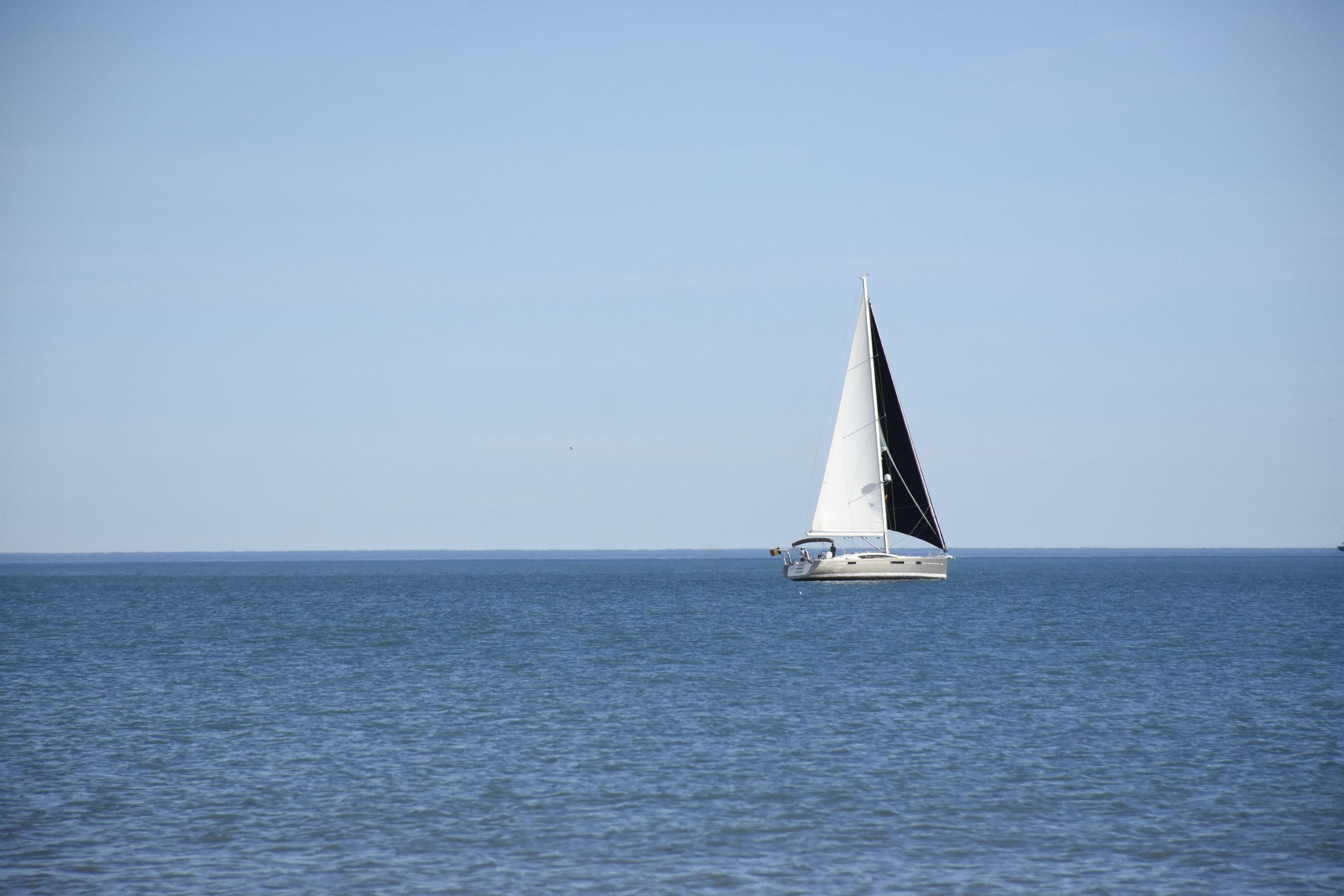 A single white-sailed yacht on pale, calm water under a soft high sky