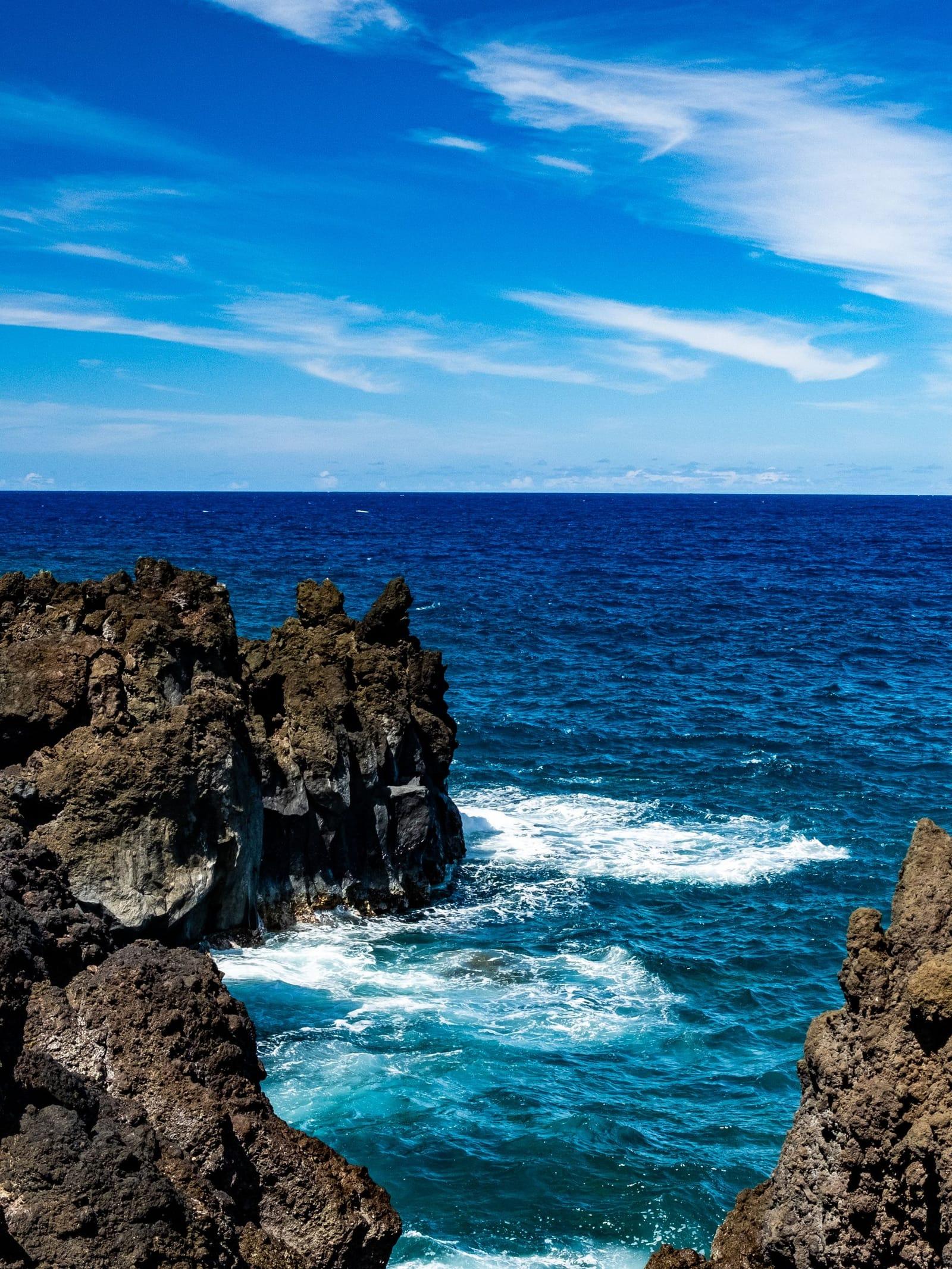 Dark lava rocks meeting bright blue ocean on the Hana coast under a clear sky