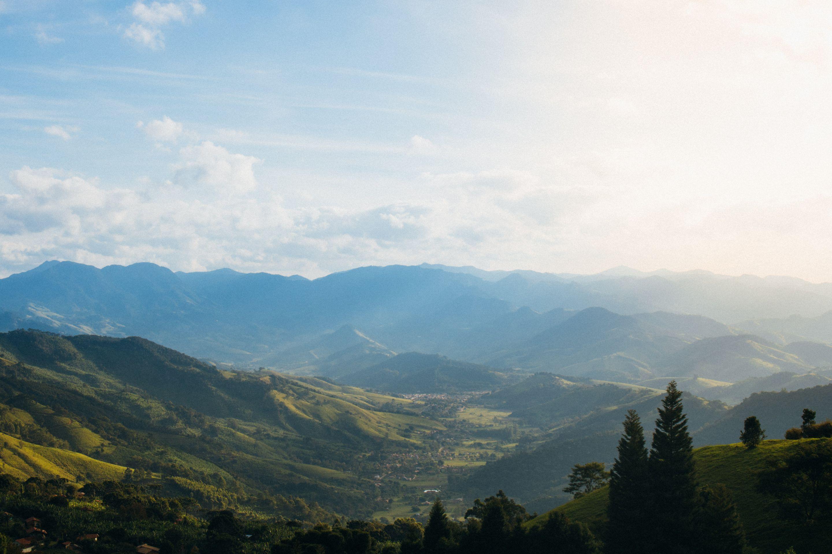 Green wooded hills receding in layers into pale haze under a bright sky