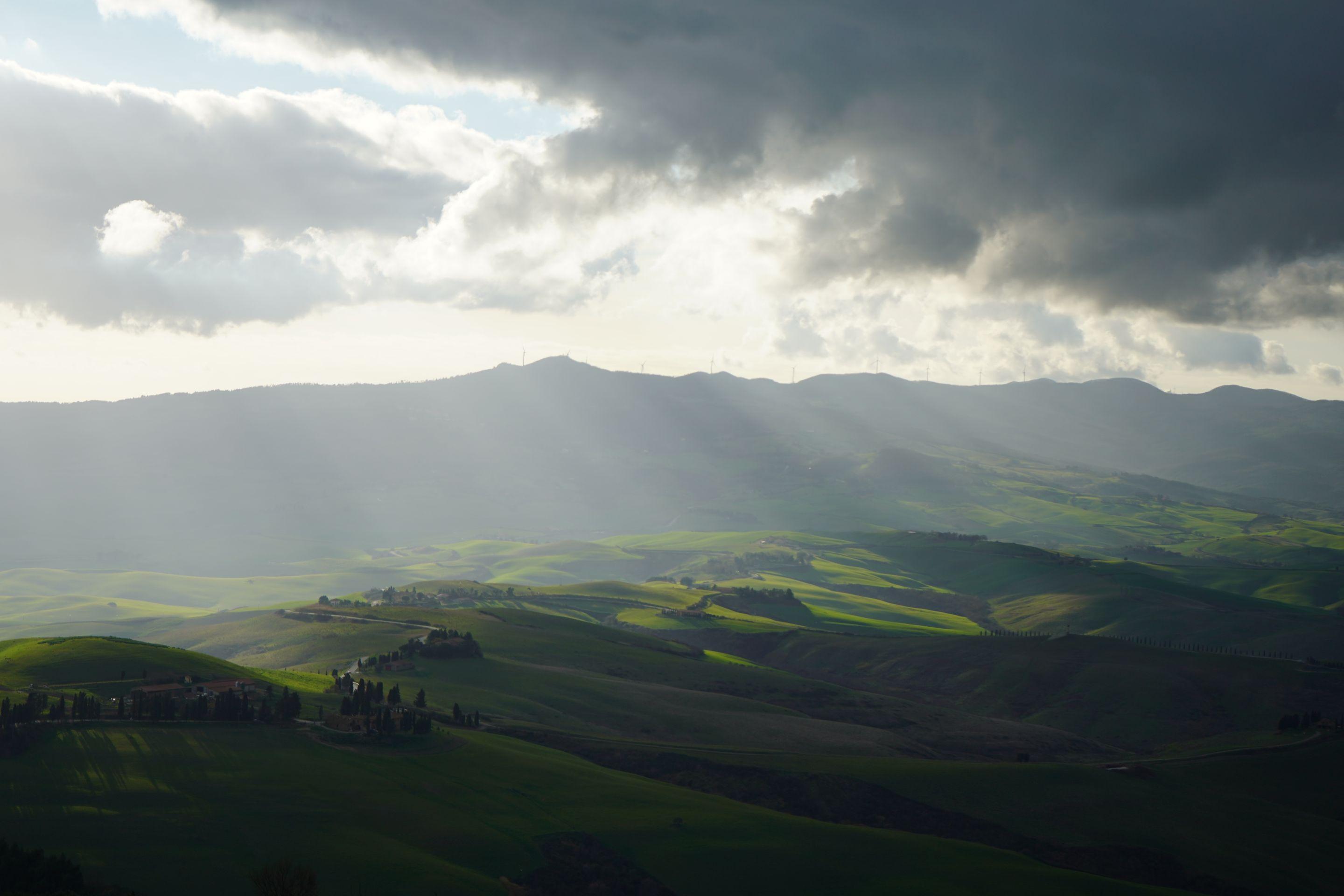 Shafts of sunlight breaking through cloud onto green farmland below