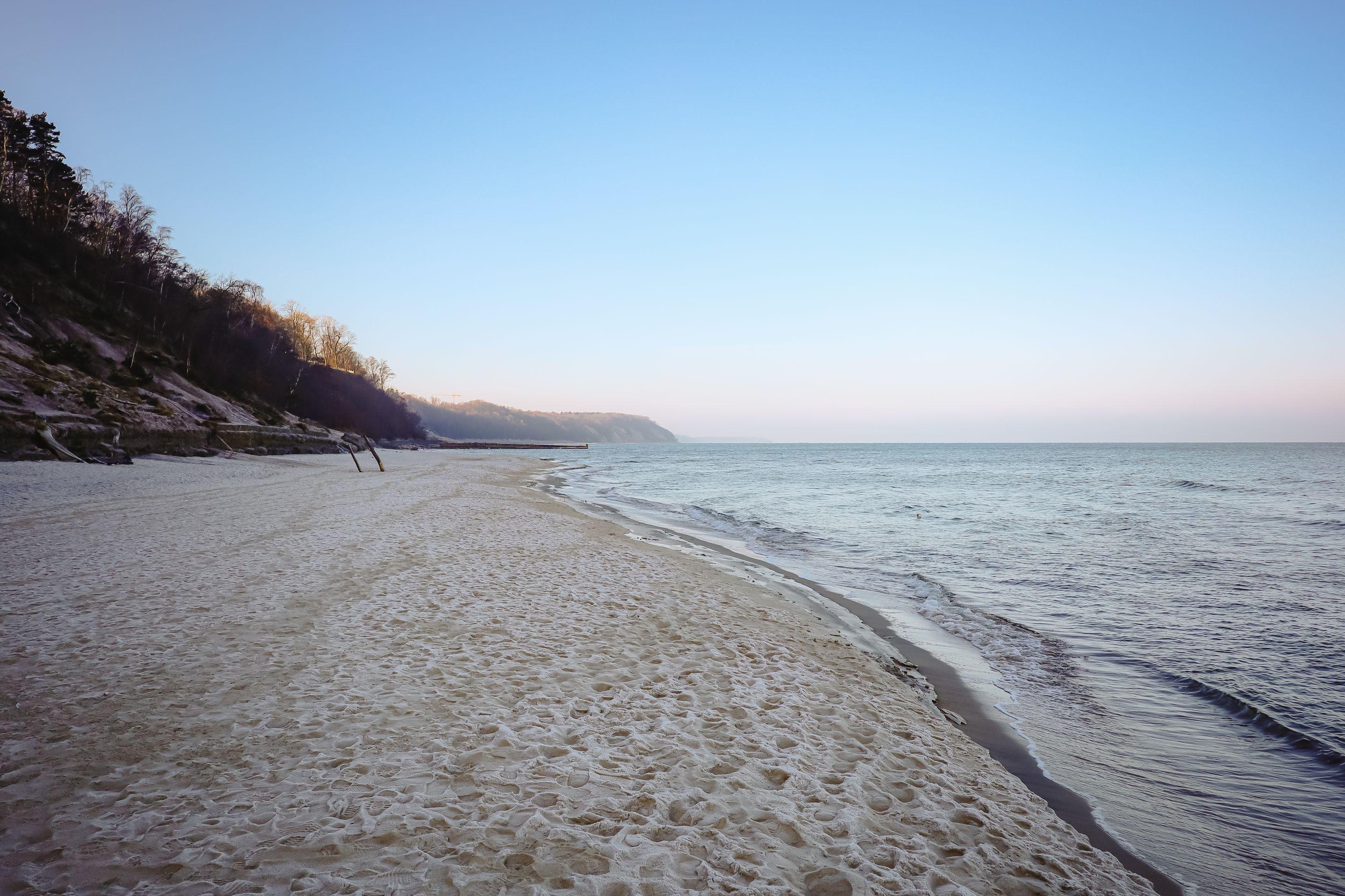 A pale empty beach and gentle surf under a soft blue morning sky