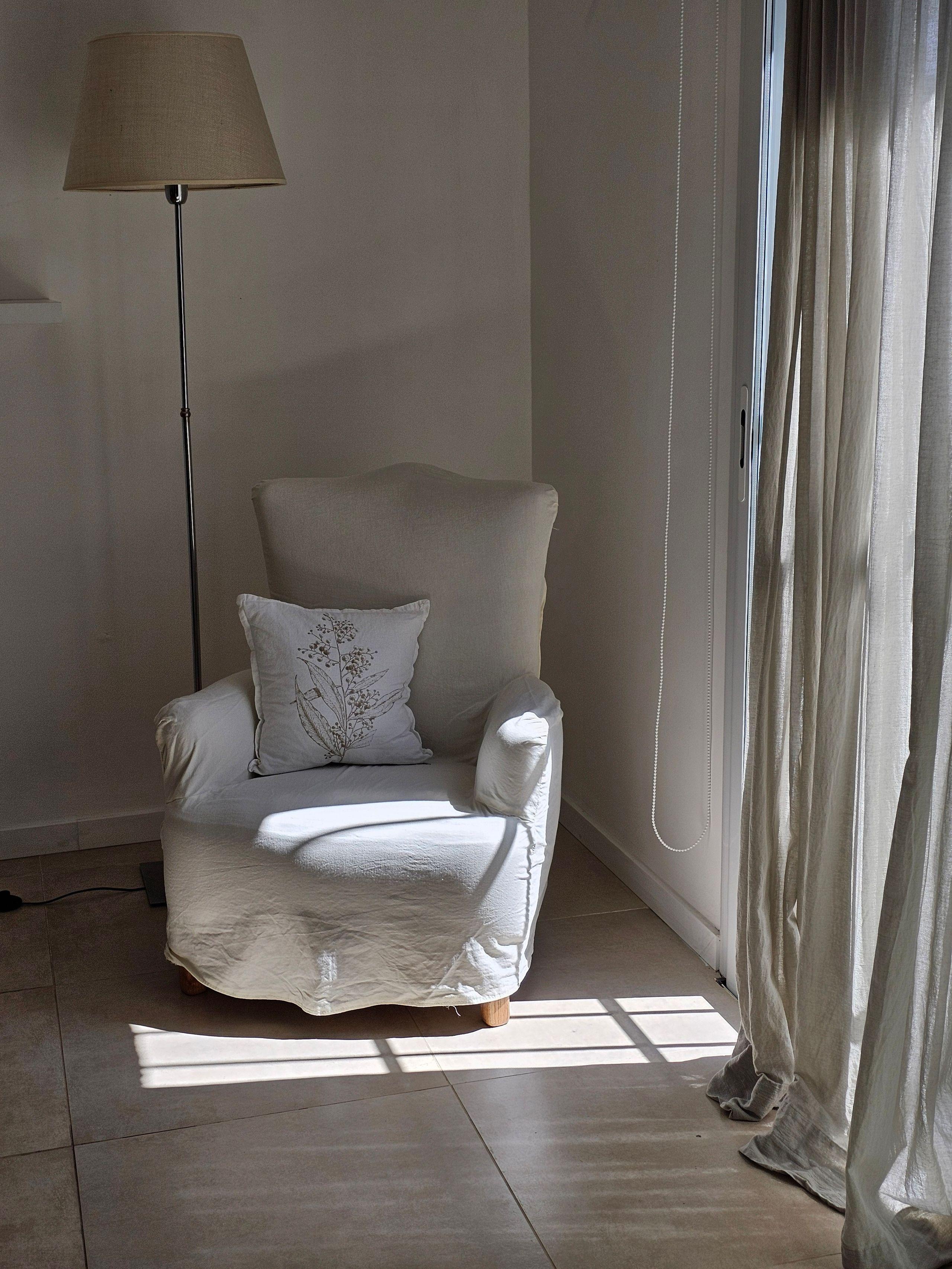 An empty armchair beside a tall window with soft morning light coming through