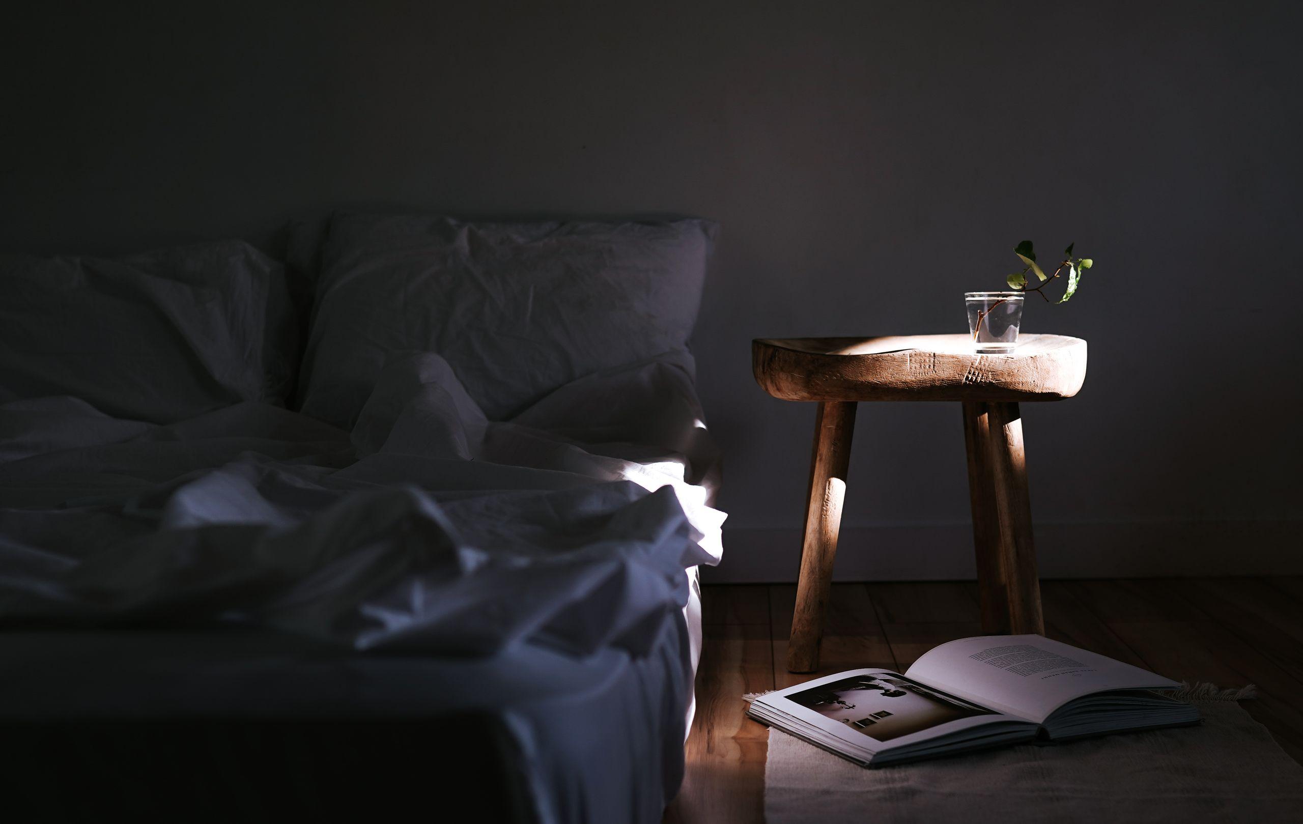 A sunlit, simply furnished bedroom with warm wood, linen bedding, and a potted plant by the window