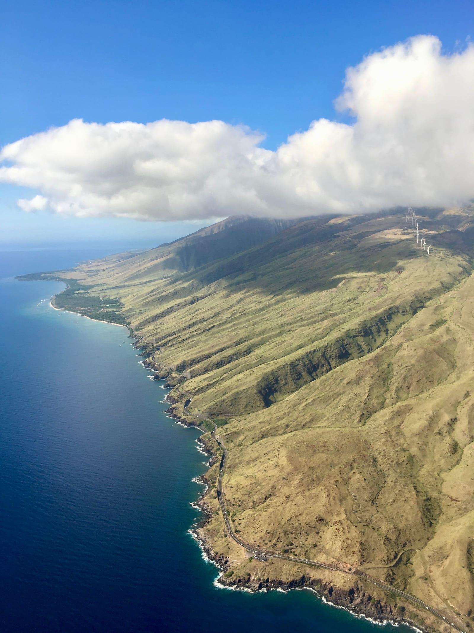 Maui's coastline and mountain slopes from above under a blue sky