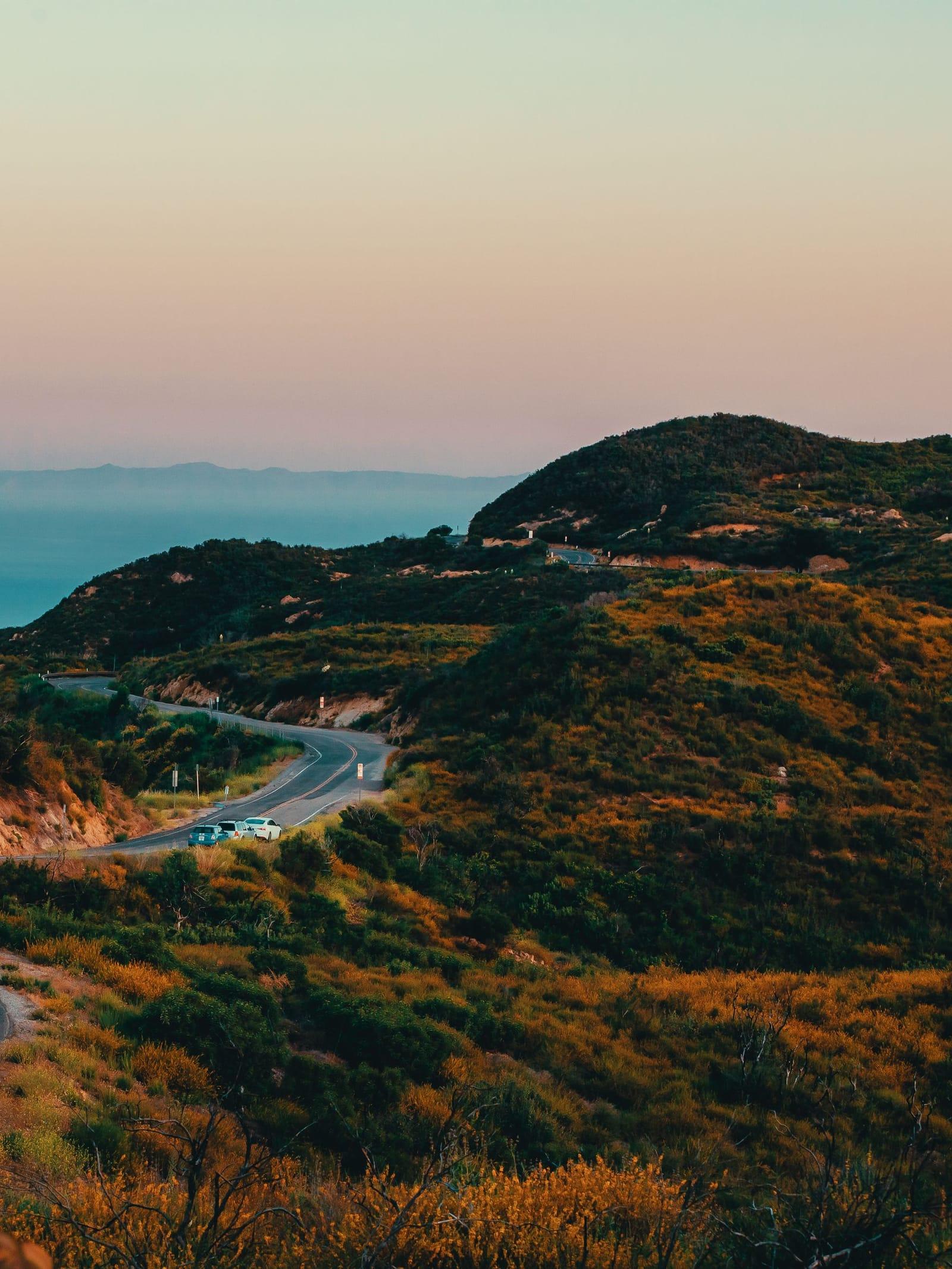 A road winding through green coastal hills toward the ocean