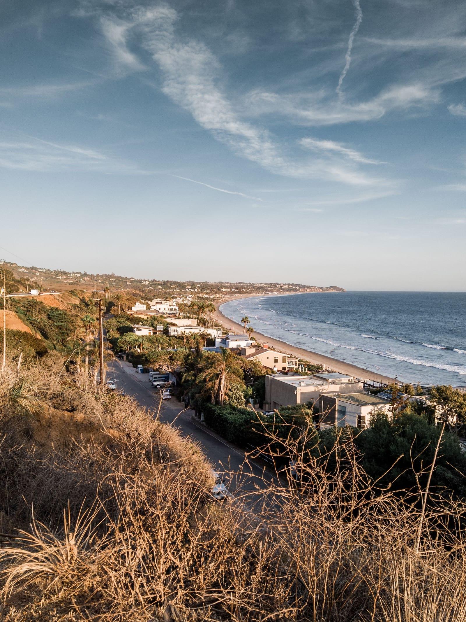 The Malibu coastline seen from a dry hillside, homes along the bluffs above a long beach