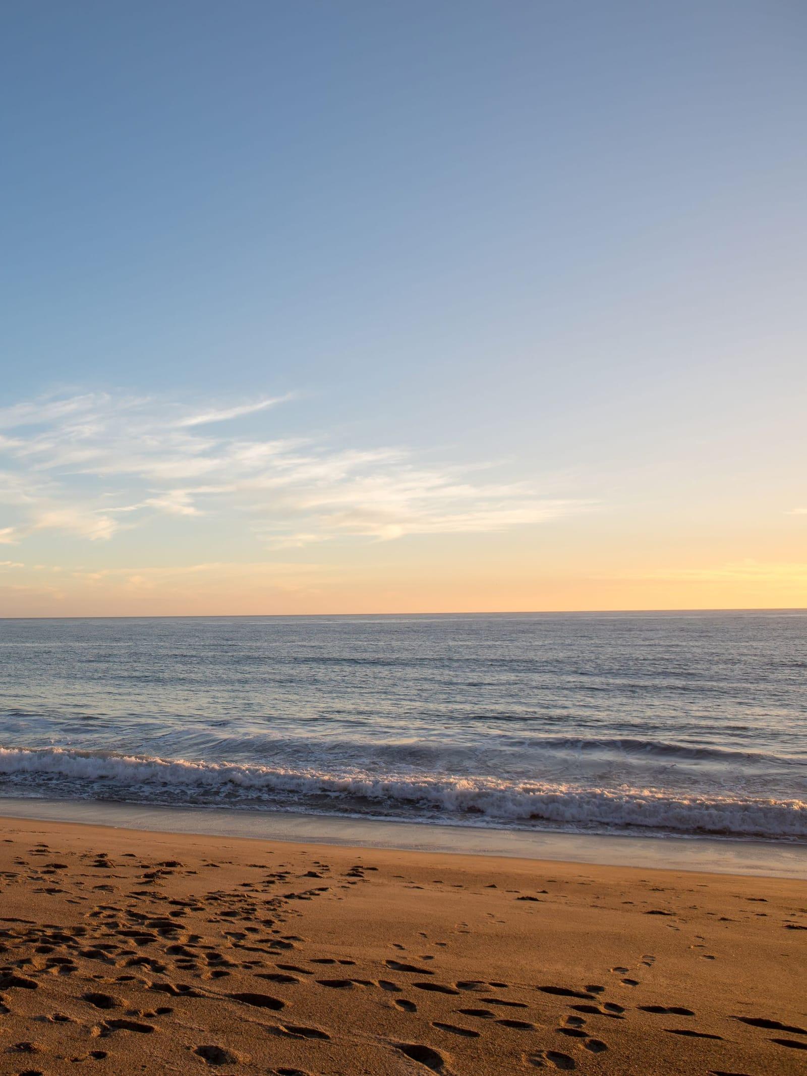 Calm ocean and footprints on the sand at golden hour