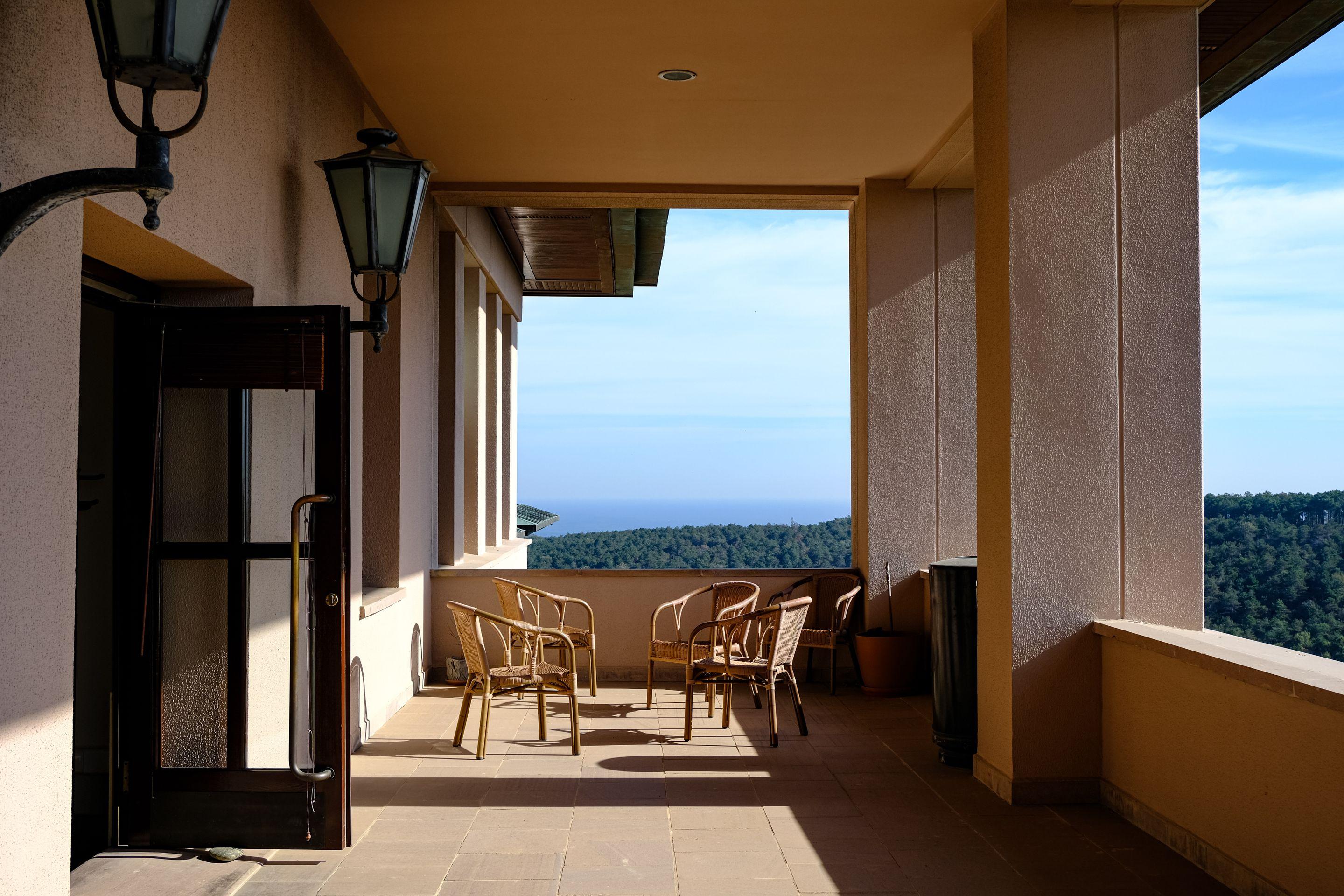 An open, sunlit gallery walkway with arches looking out over trees to the sea