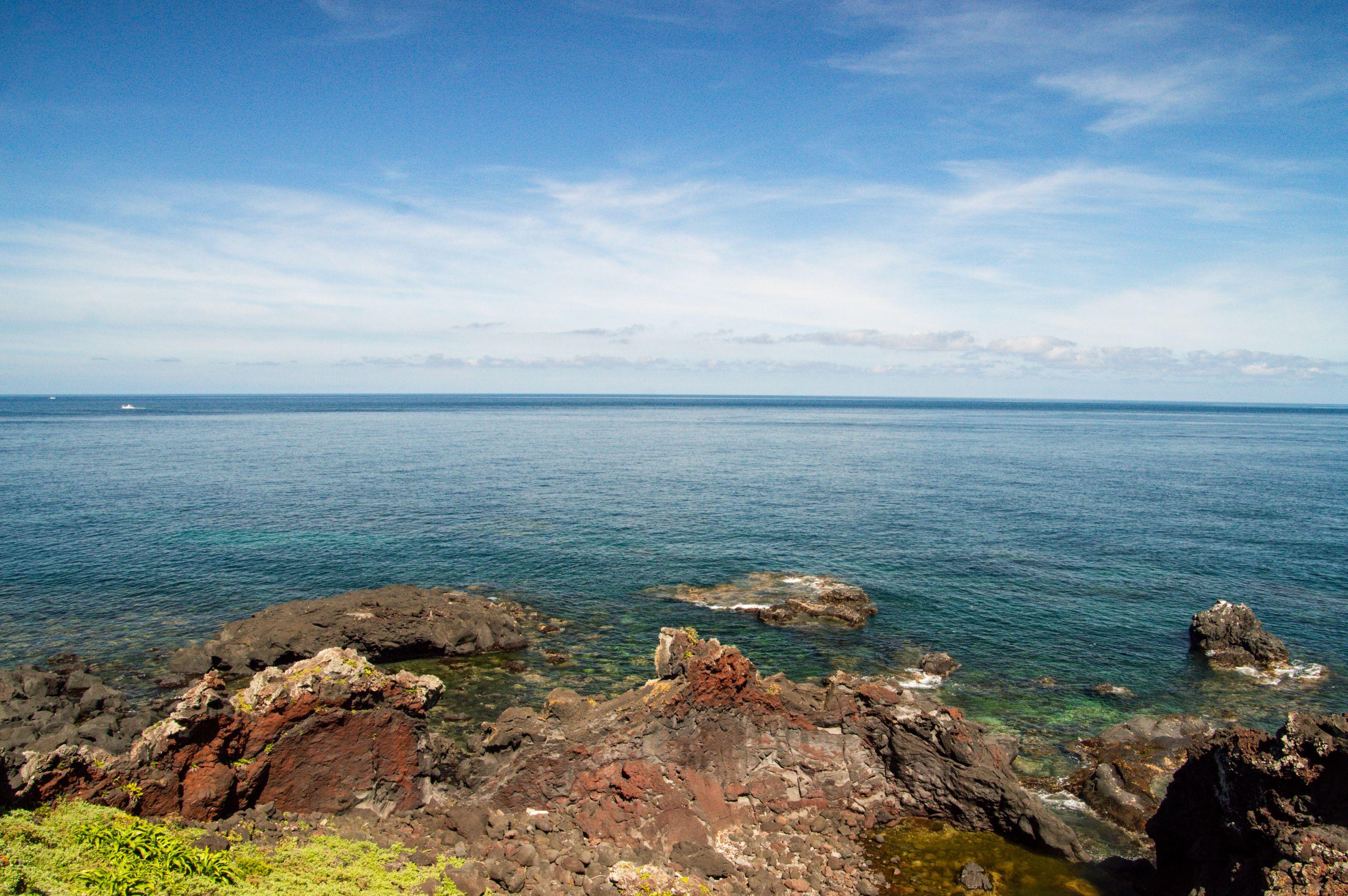 A rocky shoreline below a wide blue sea and a sky streaked with high cloud