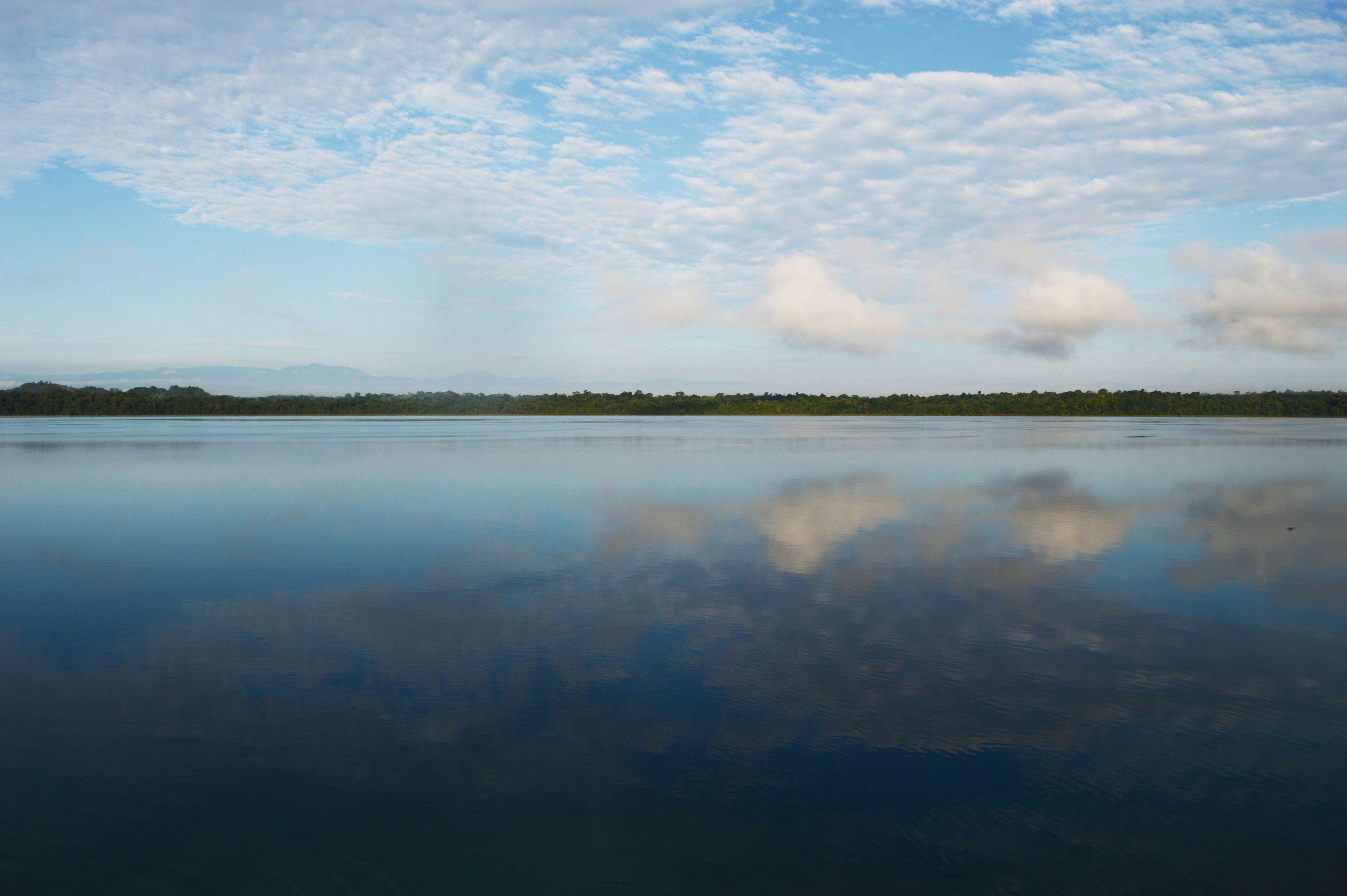 A still lake reflecting a bright sky and a low line of trees on the far shore