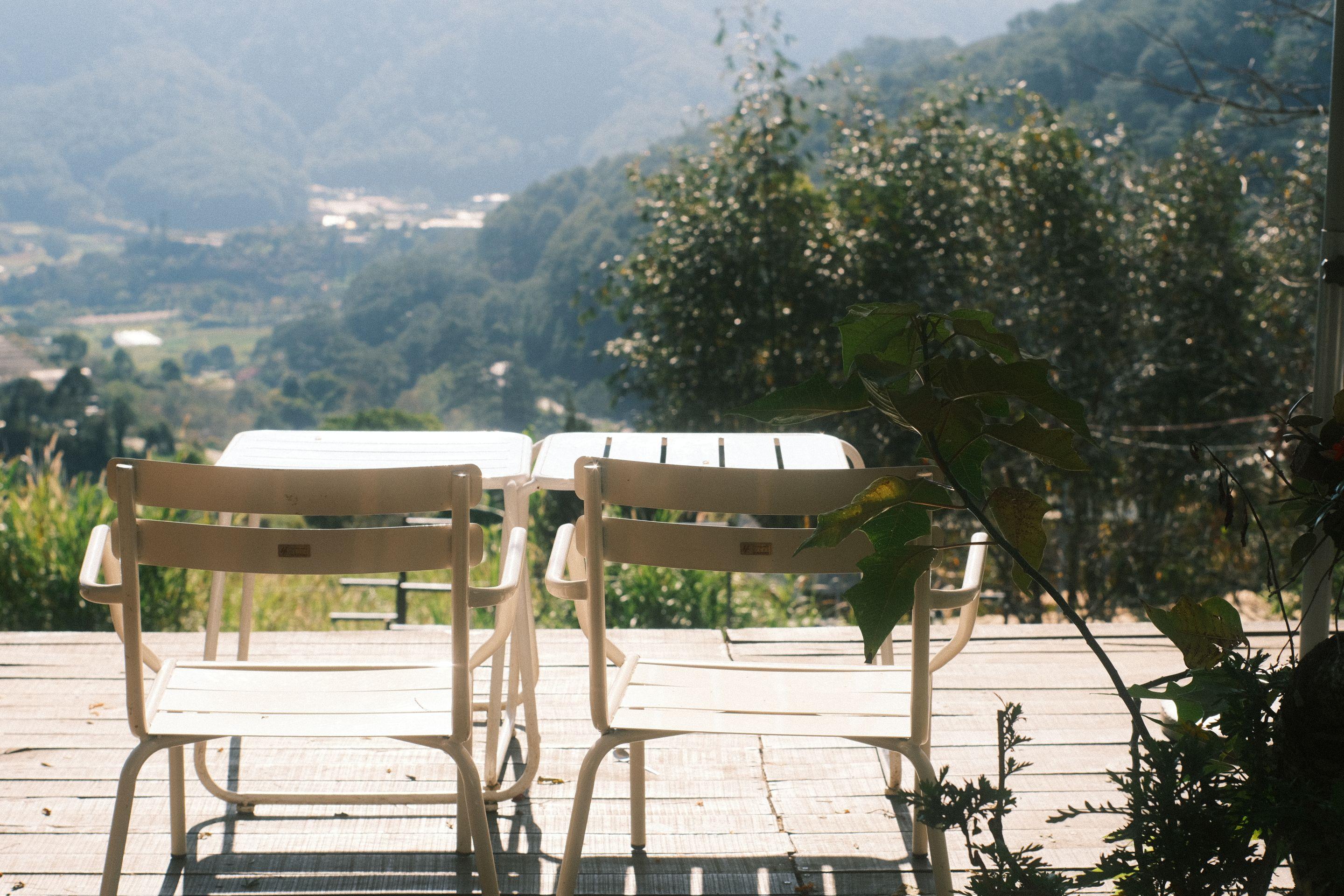 A small table and chairs on a sunlit terrace looking out over a green valley