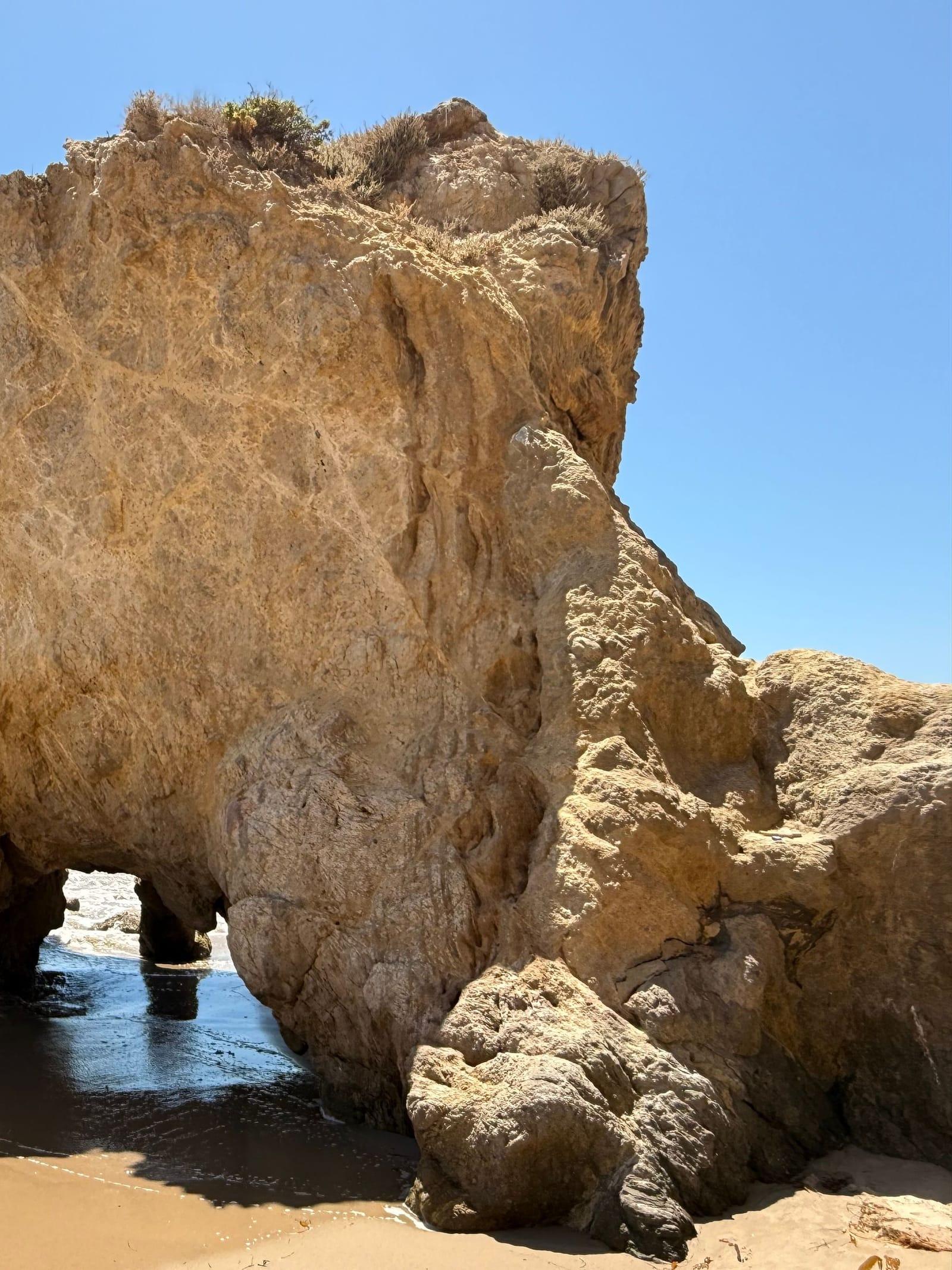 A sandstone rock arch on the sand at El Matador State Beach under a clear sky