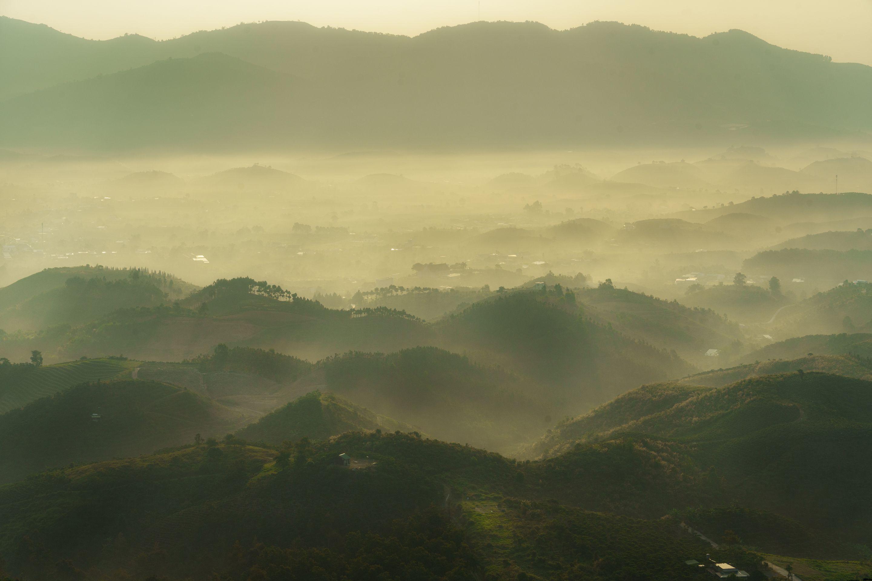Layered green hills receding into pale morning haze under a bright high sky