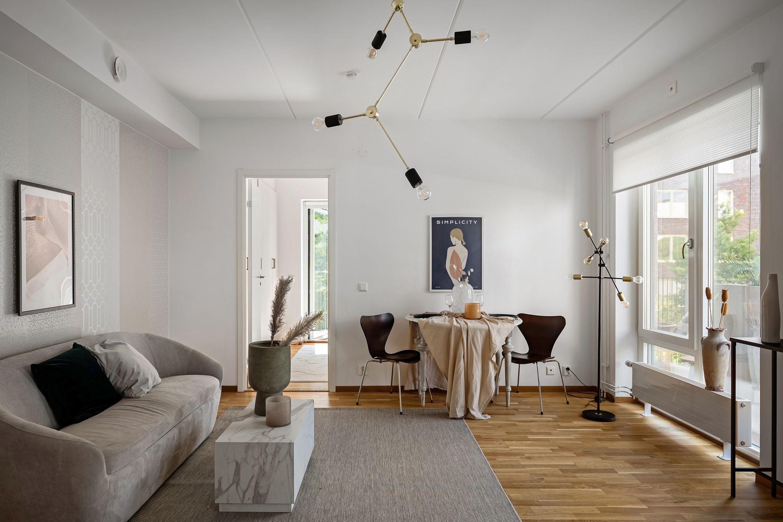 A bright, minimalist sitting room with warm wood floors, natural daylight through tall windows, and simple furnishings