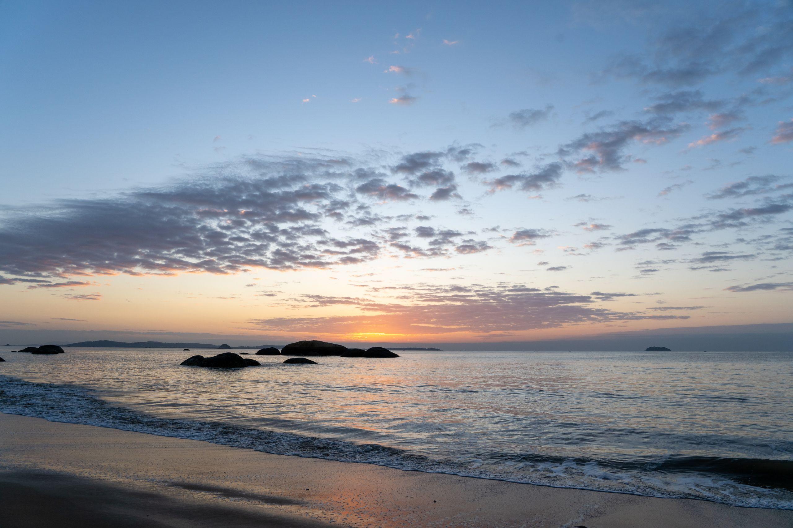 A calm ocean at sunrise with still water and soft pastel light along the horizon