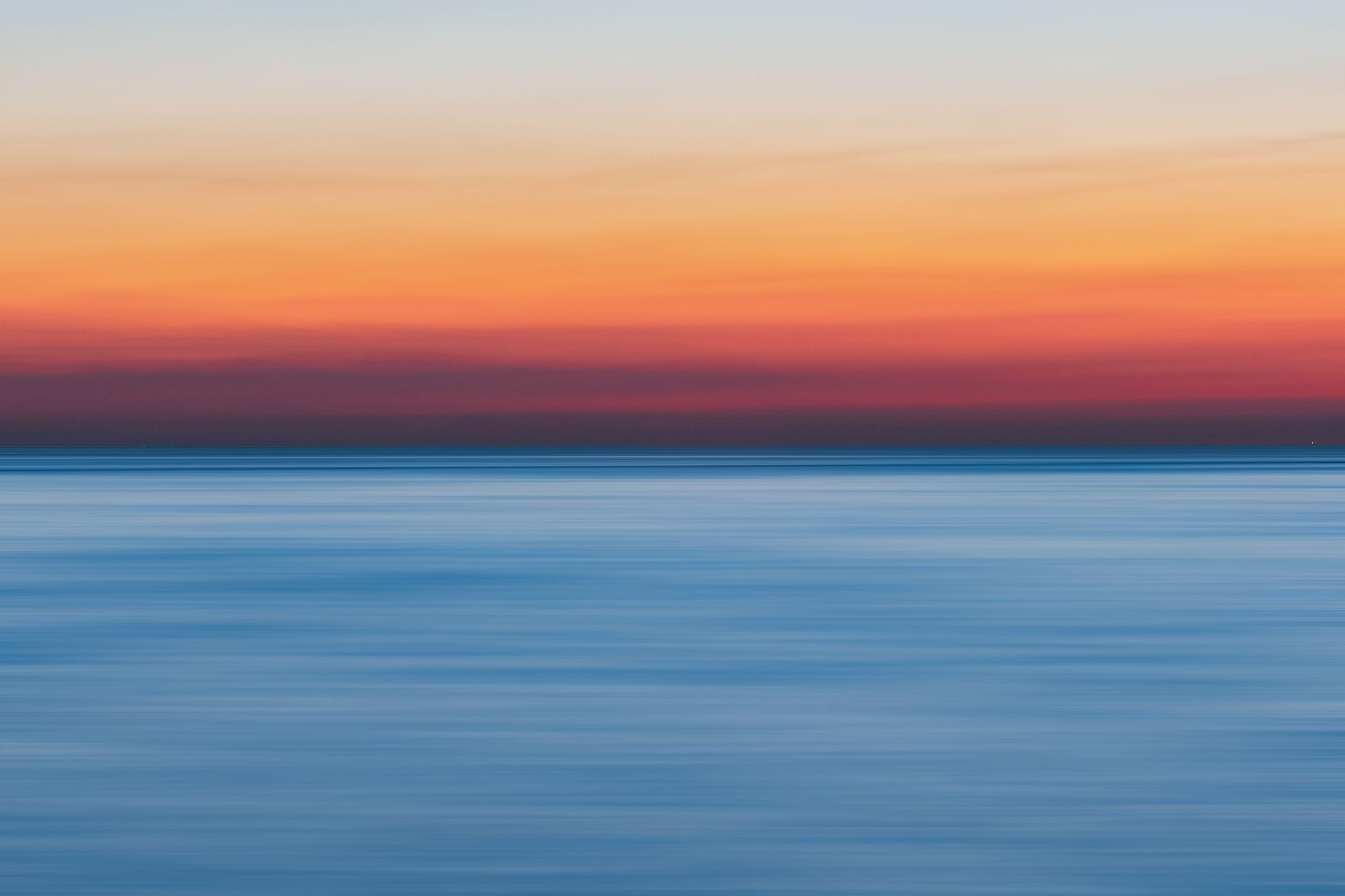 A calm, still ocean under a warm sunset sky fading from orange to blue