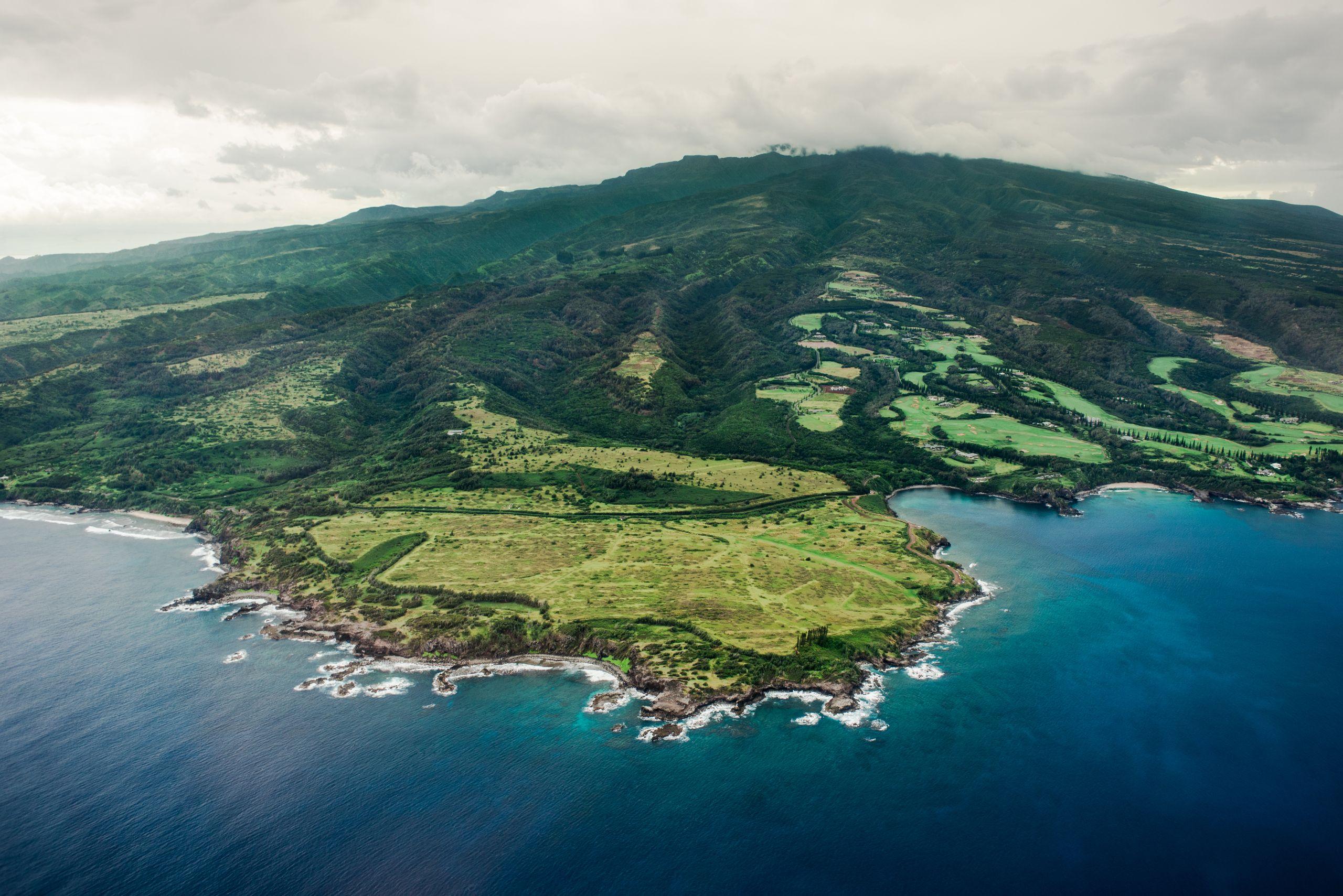 Aerial view of a green headland meeting deep blue ocean under a dramatic cloudy sky