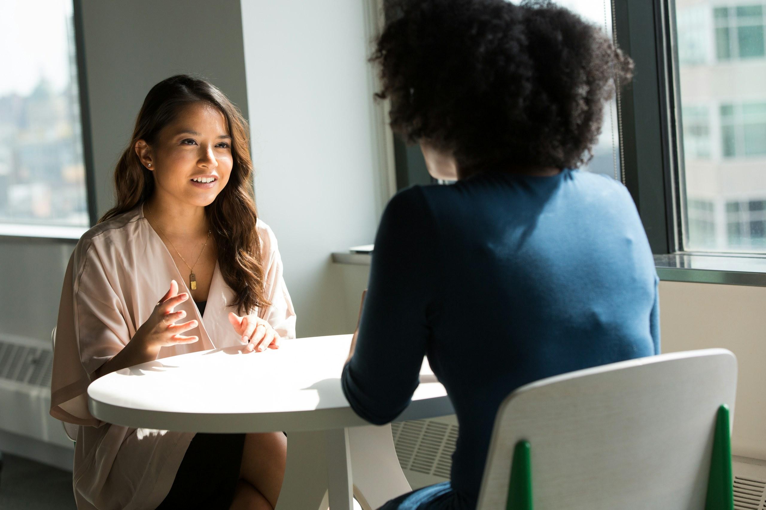 Two people in conversation across a small table in a daylit office