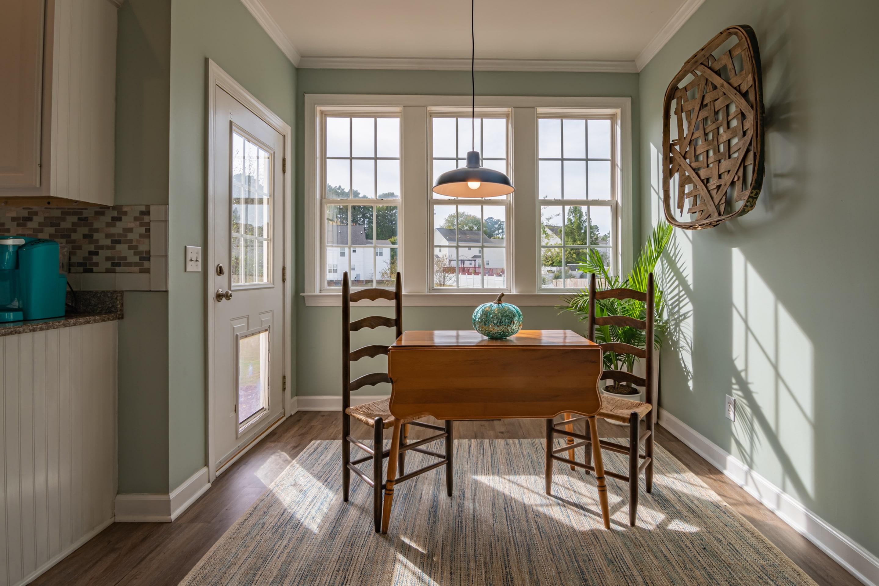 A wooden table and chairs in a bay window, morning light across the floor