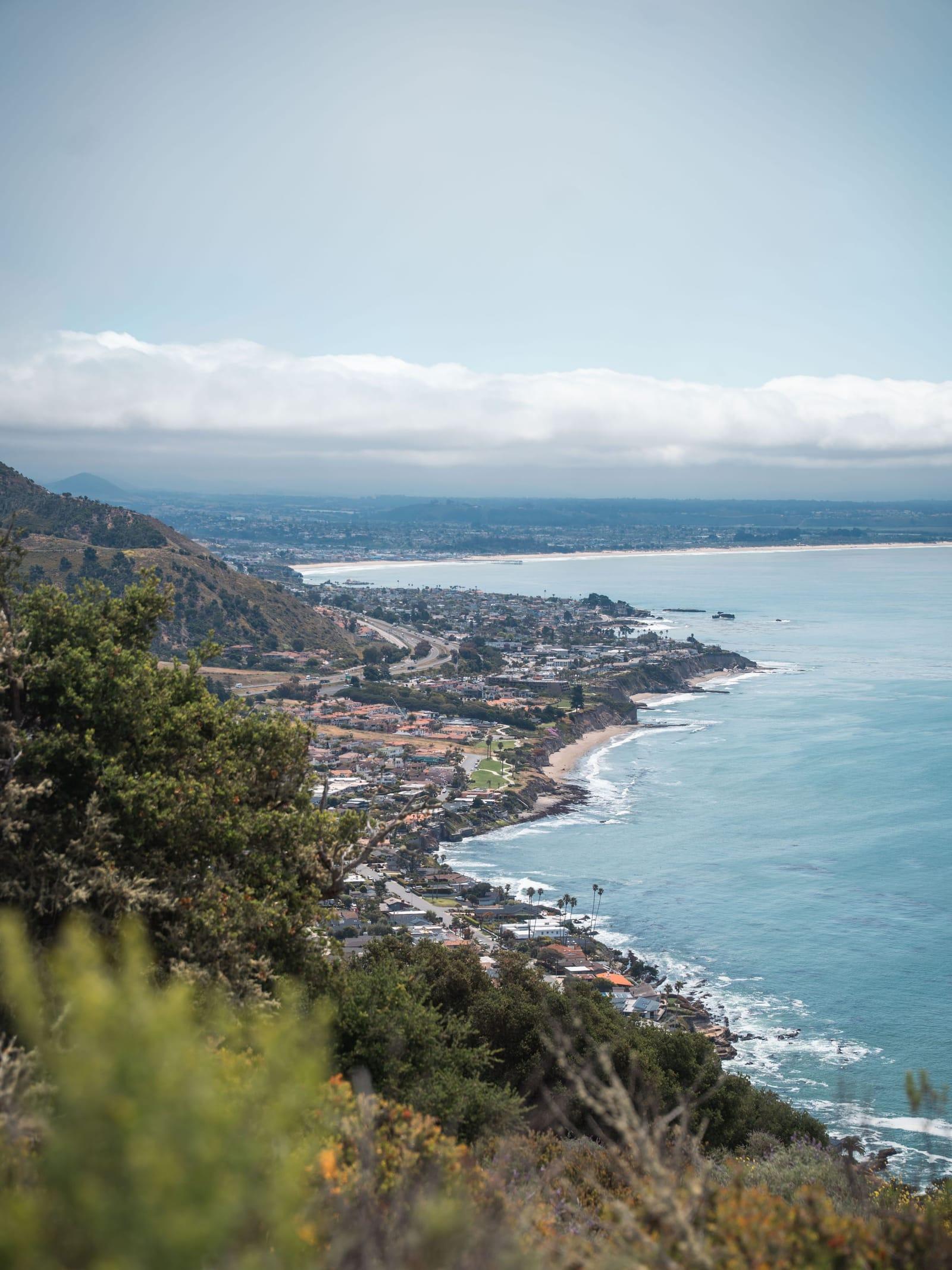 The Malibu coastline seen from a green hillside, surf breaking along the shore below