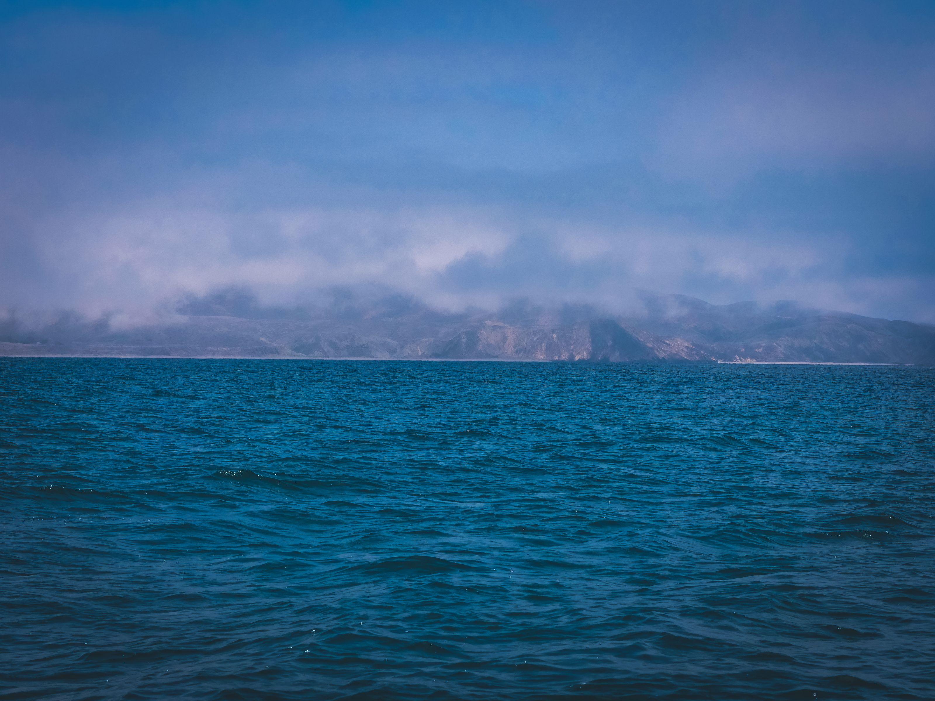 Marine layer breaking over a coastal mountain range across deep blue Pacific water