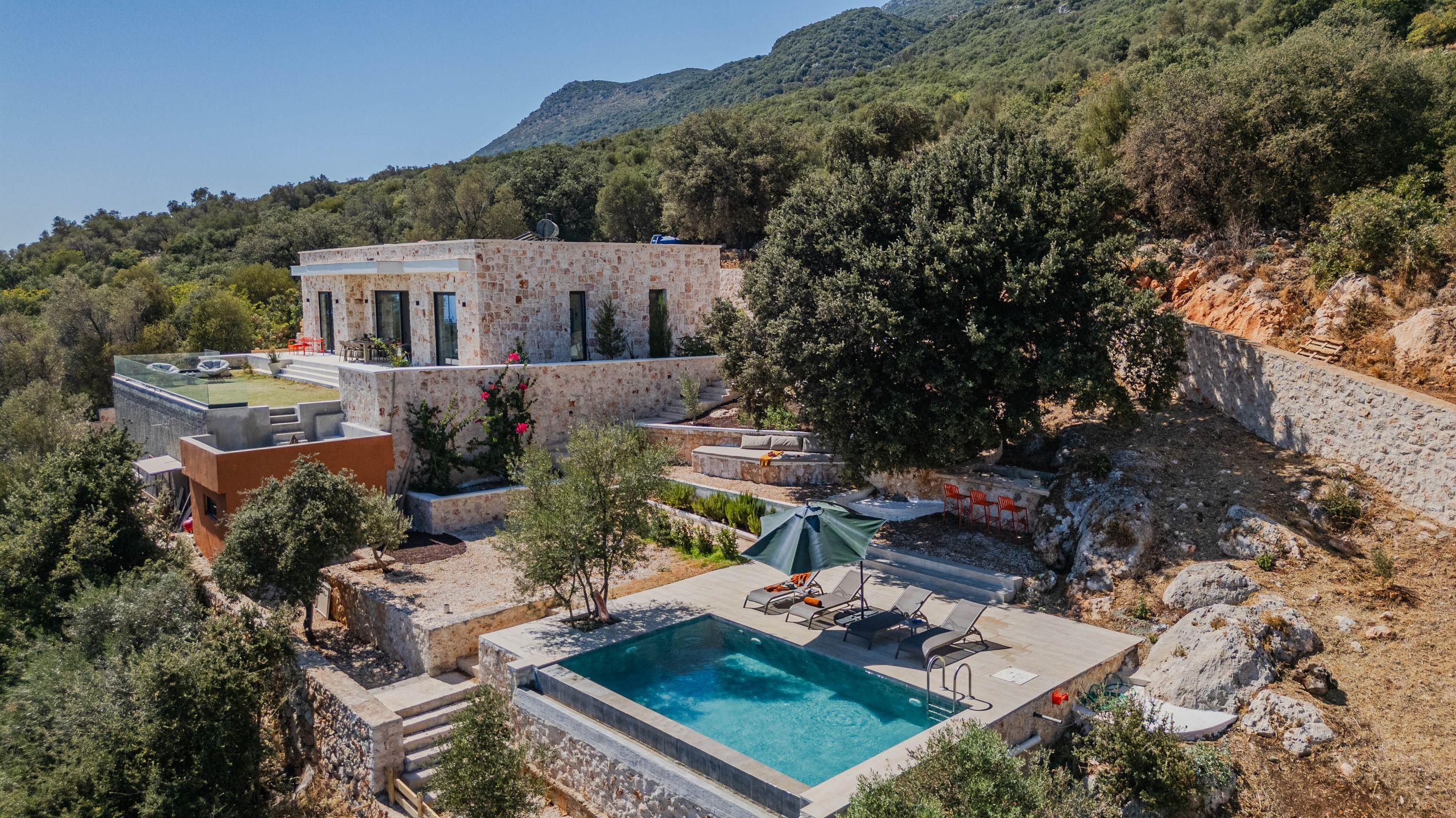 A stone villa with a private pool surrounded by hillside greenery and open sky