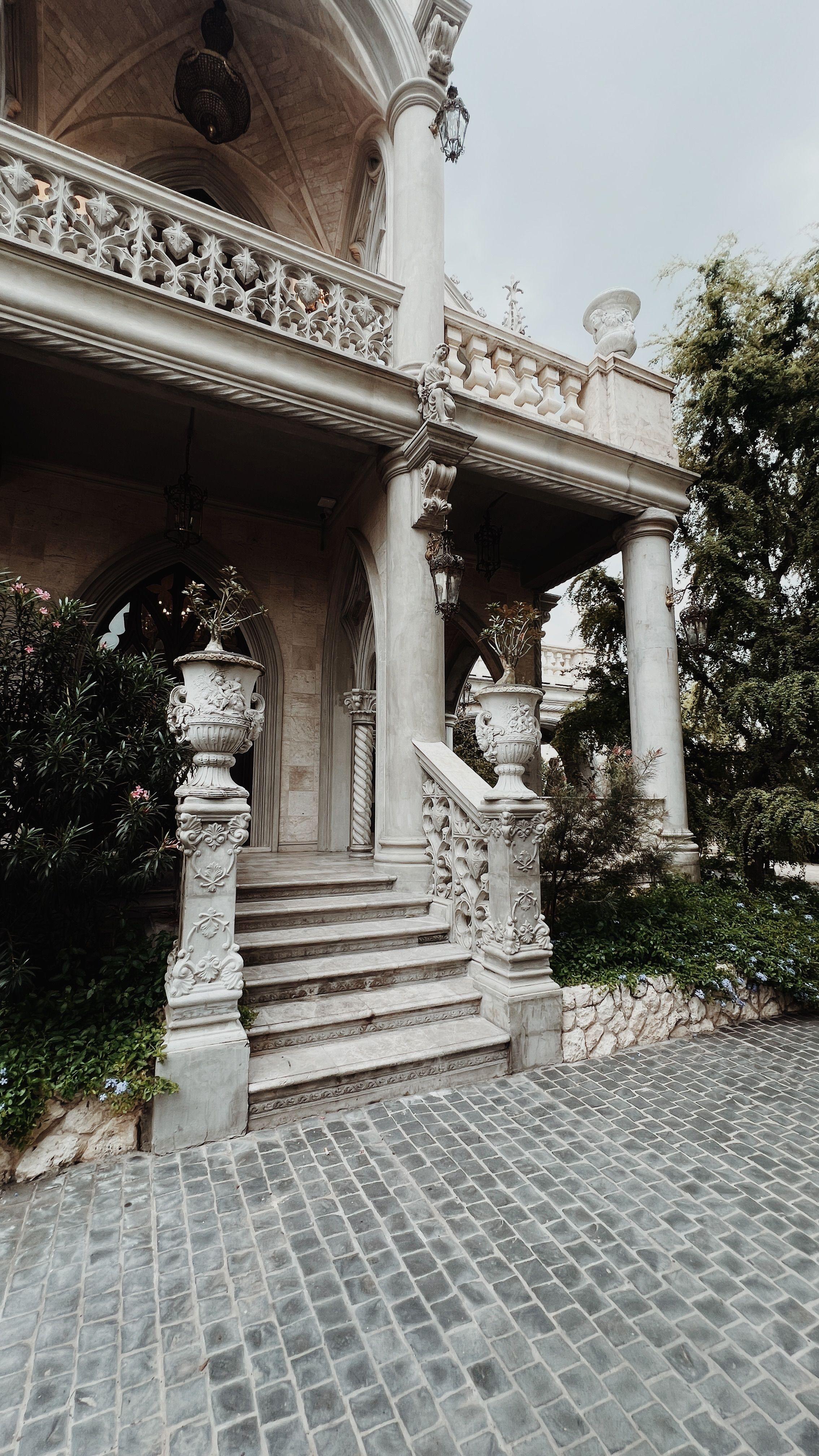 A grand classical mansion entrance with carved stone columns, urns, and a sweeping staircase