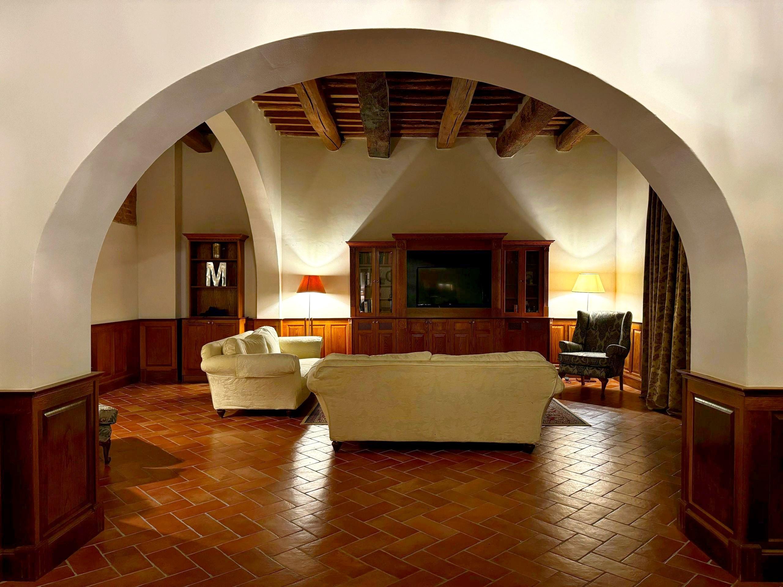 A warm Tuscan villa sitting room with a vaulted beamed ceiling, soft lamplight, and classic sofas