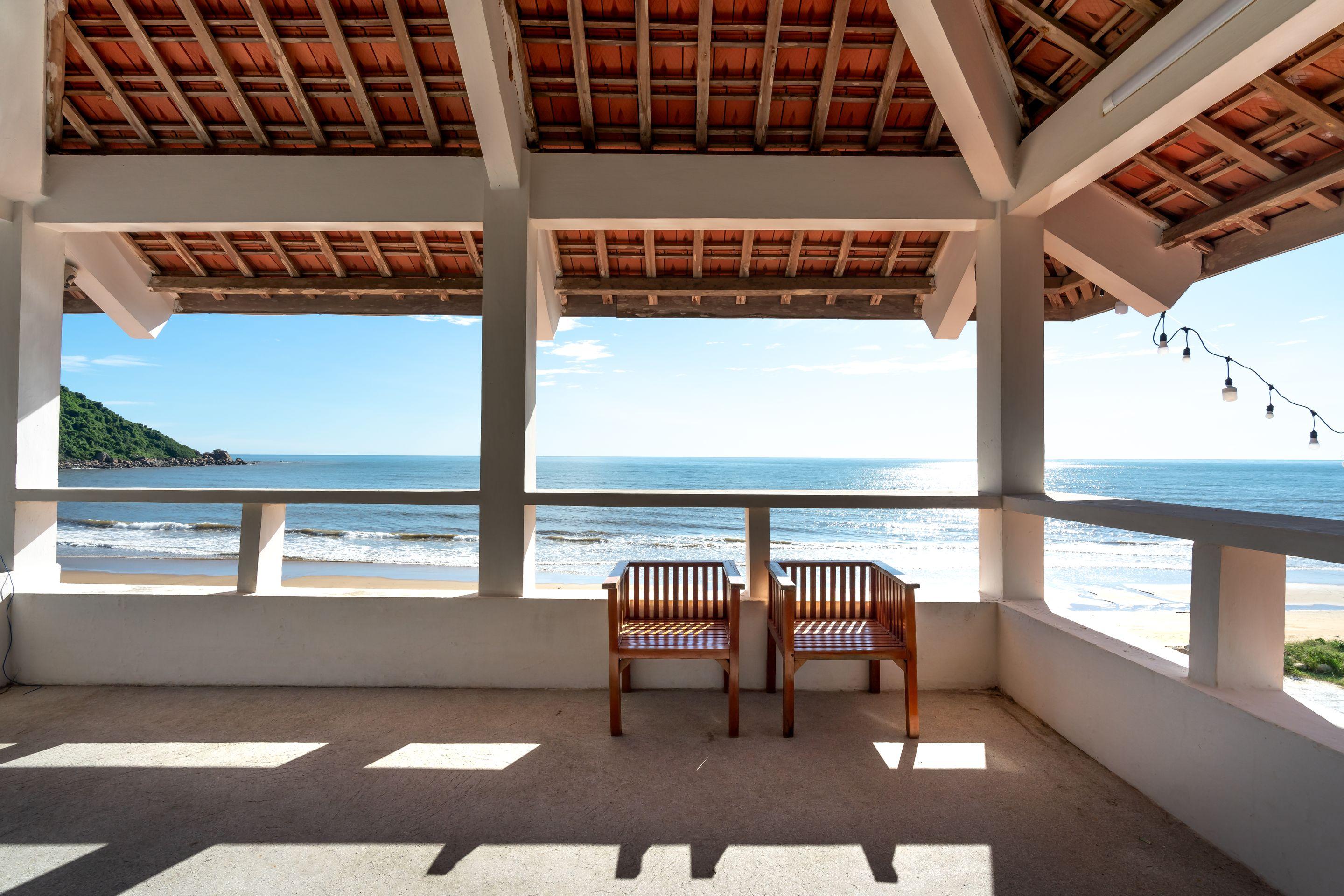 Two wooden chairs under an open pavilion looking out to a bright sea