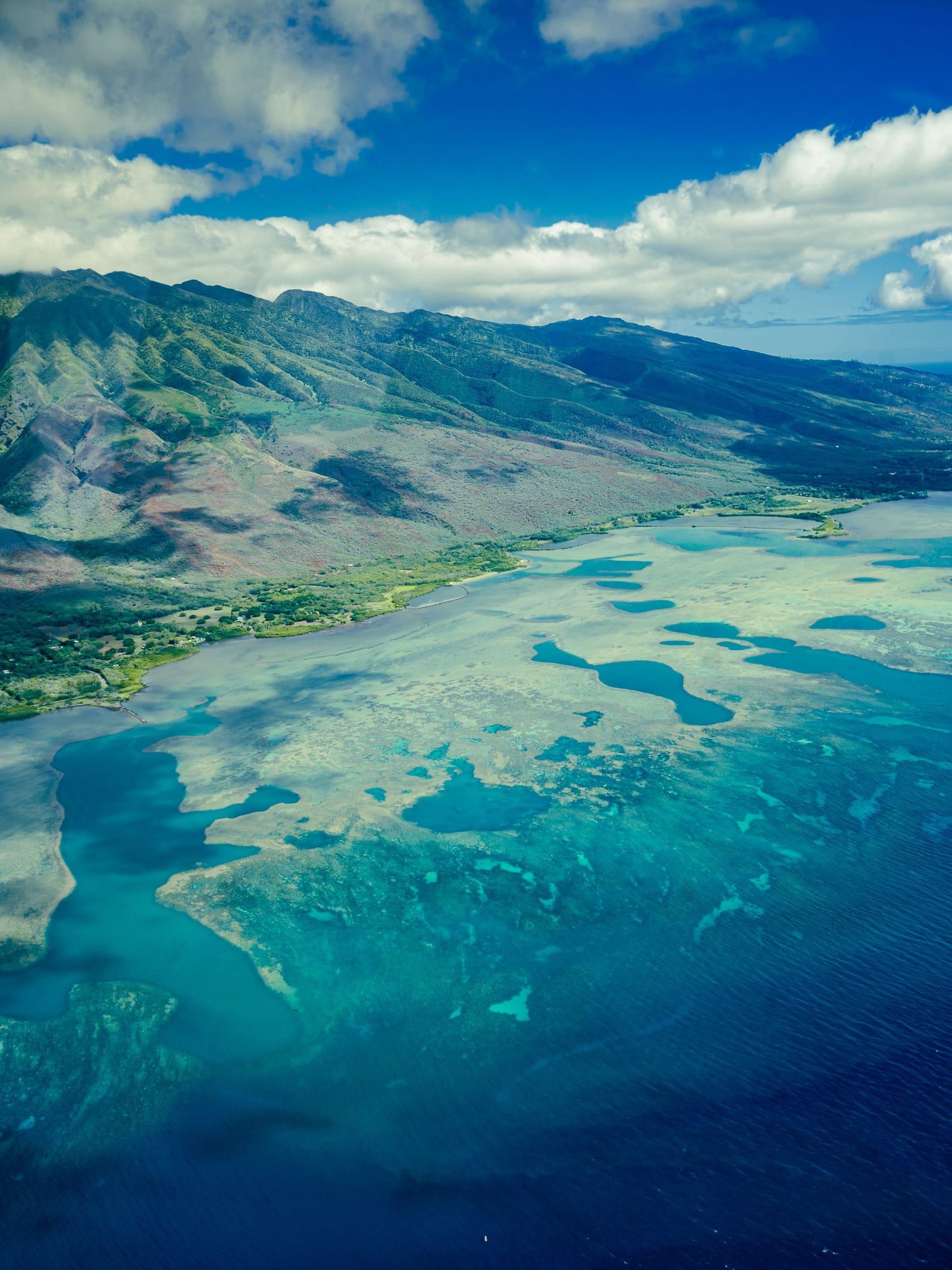 Maui's coastline from above, a turquoise reef below green mountains