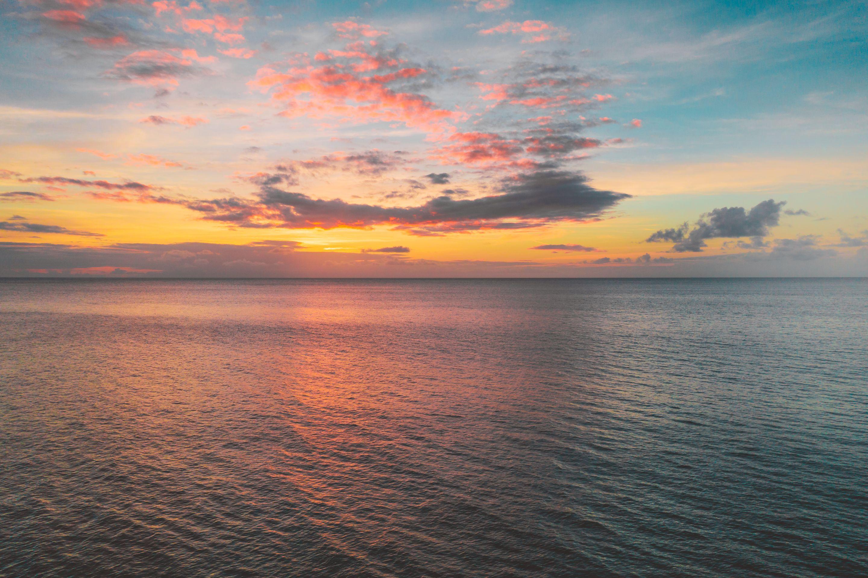 A calm sea under a pale dawn sky with soft pink cloud near the horizon