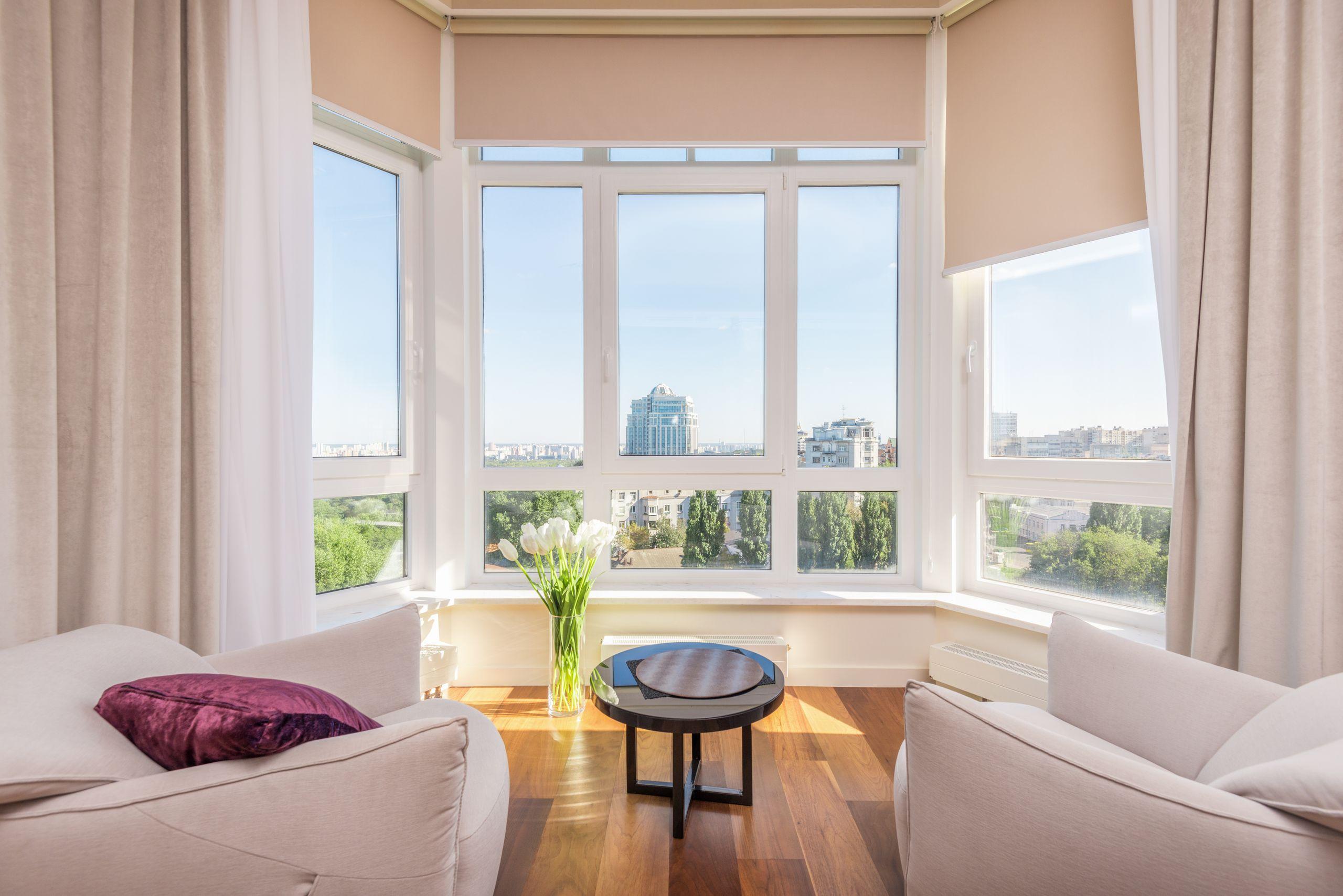 A bright, airy sitting room with white sofas and sunlight pouring through large bay windows