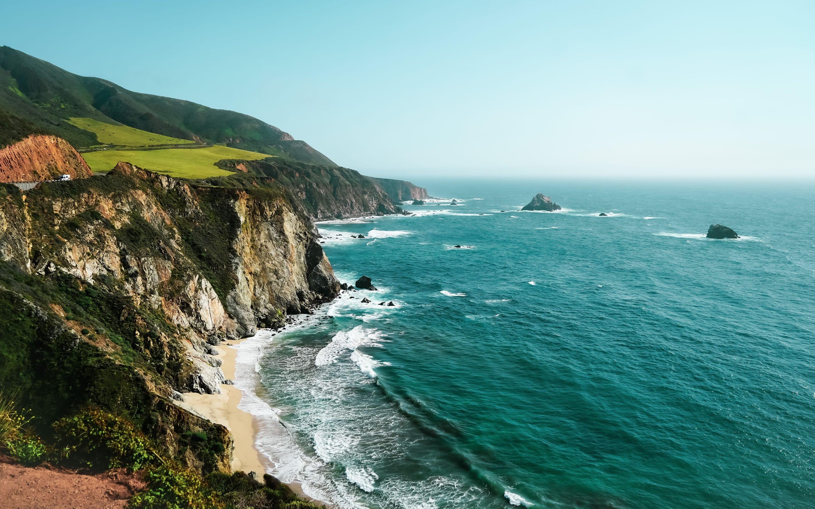 The Big Sur coast of California on a clear day, green headlands above a sandy cove and turquoise water