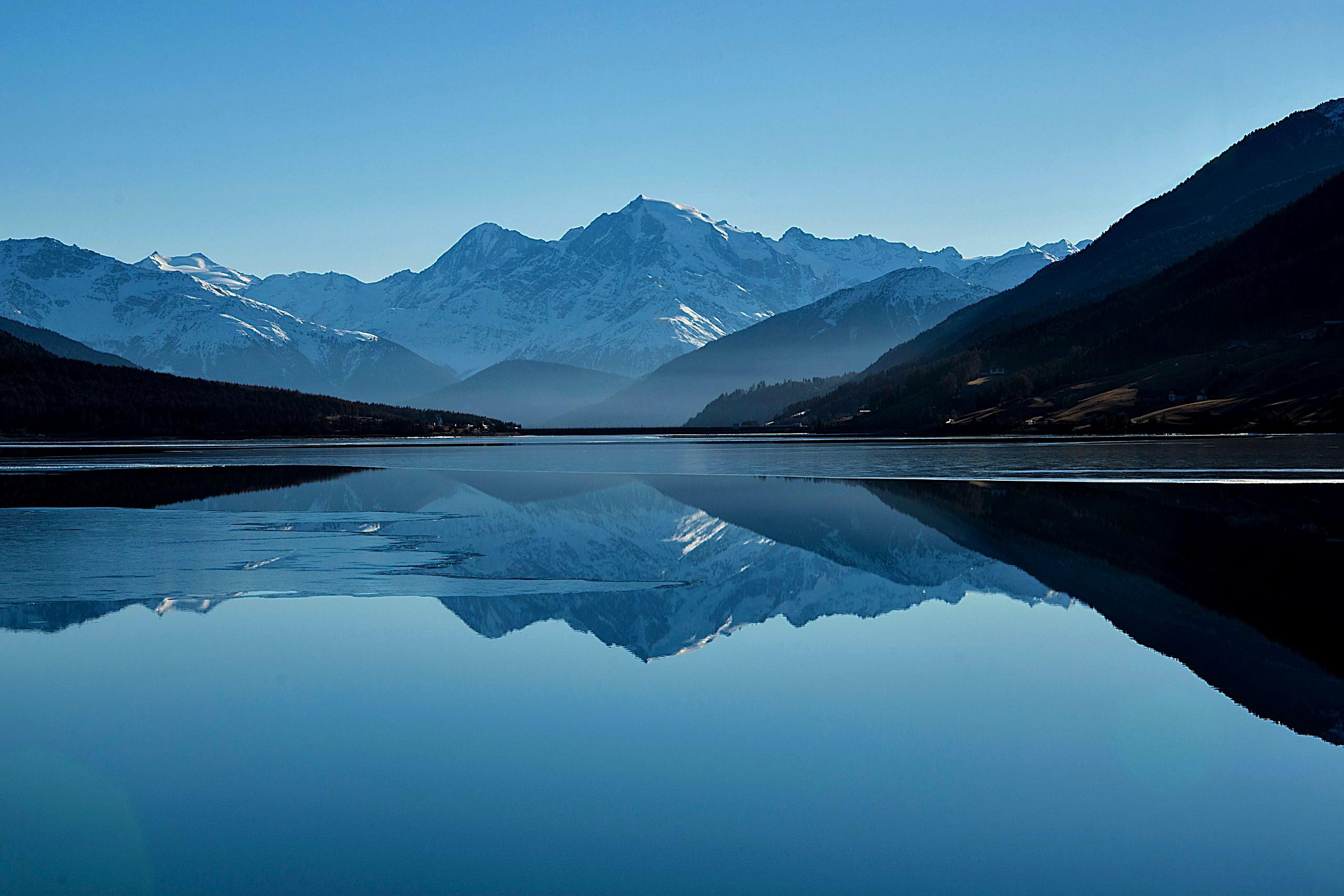 A calm mountain lake mirroring green peaks under a bright blue sky