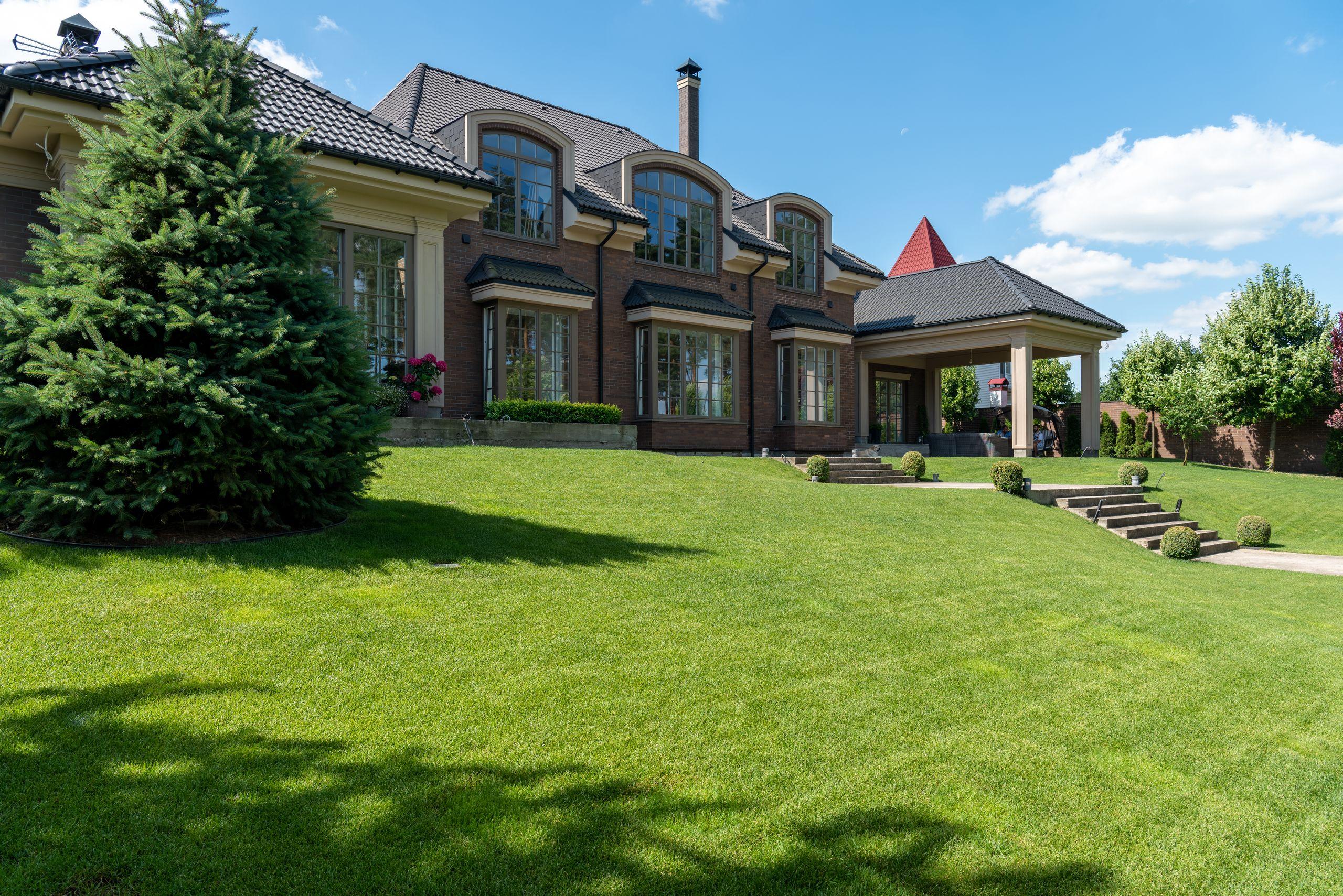 A modern luxury estate with a manicured green lawn and landscaped grounds under a clear sky