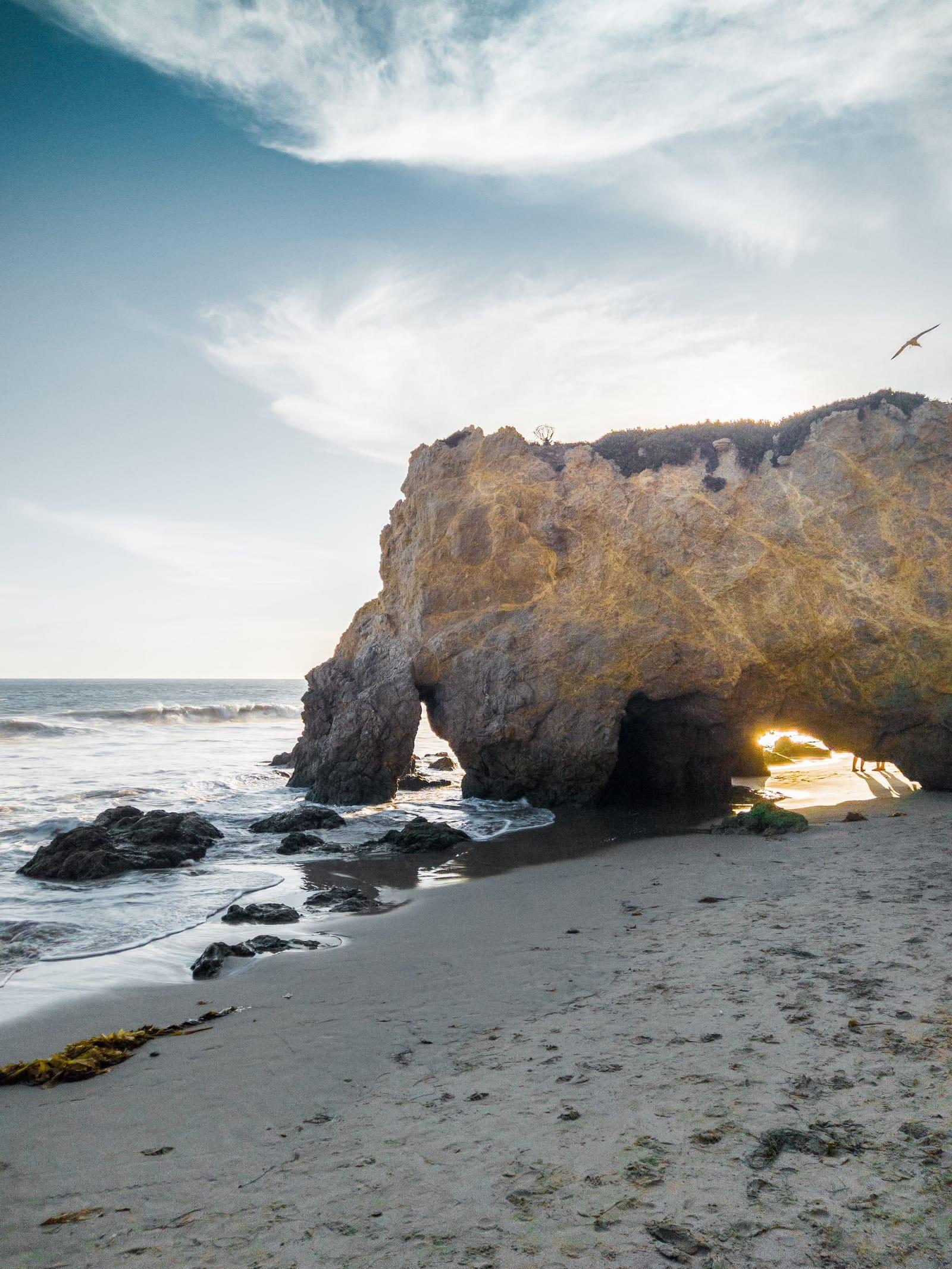 A sunlit sandstone arch on a Malibu beach under a bright sky