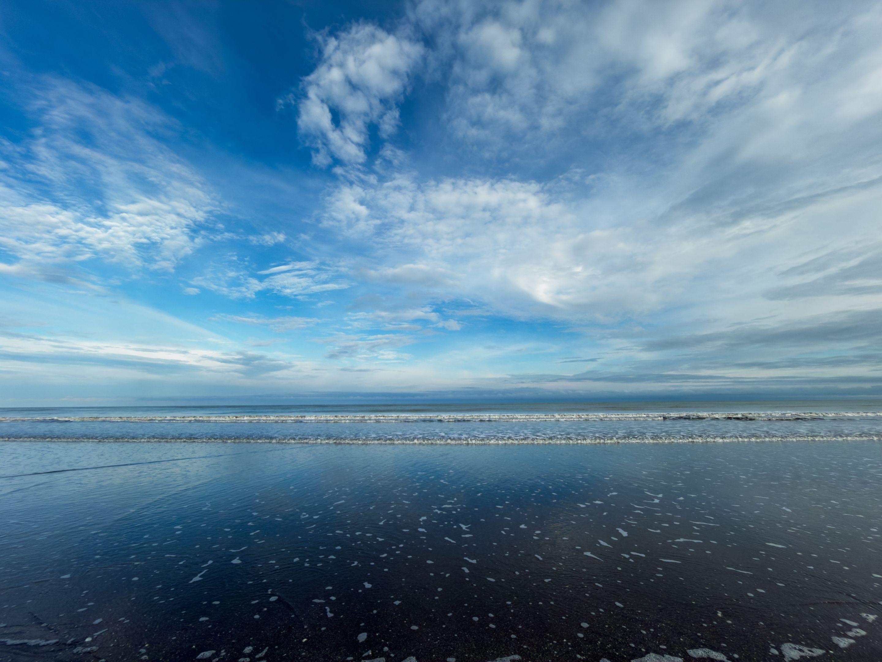 A calm ocean under a wide blue sky feathered with high cirrus