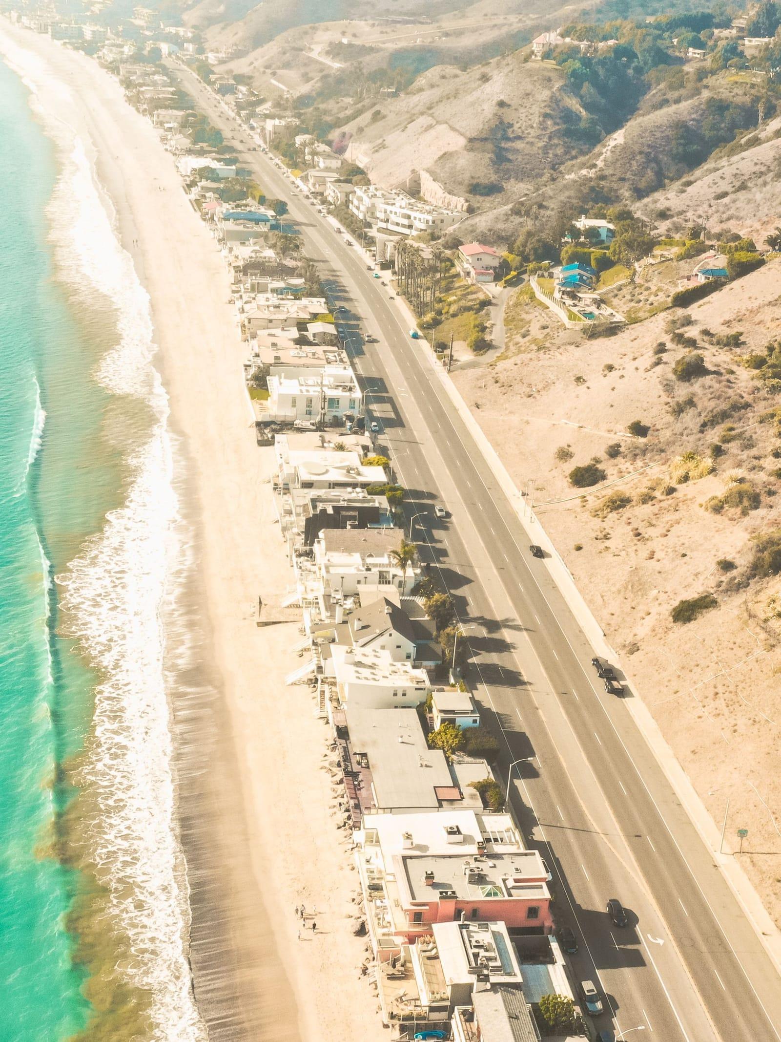Beach houses lining a long Malibu beach beside the coast highway, seen from above